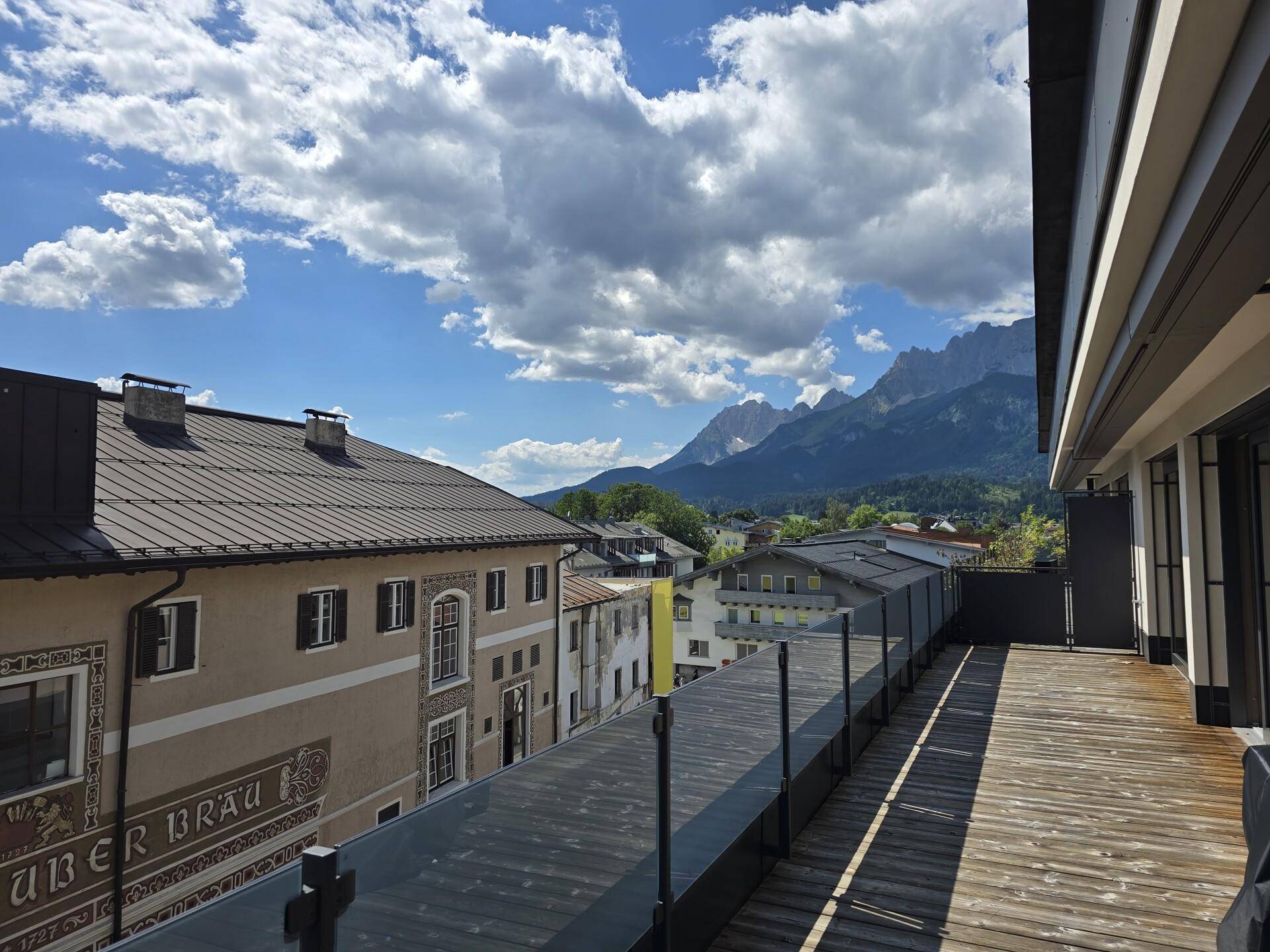 Lange Terrasse mit Holzboden und Blick auf die Stadt und die majestätischen Berge im Hintergrund.