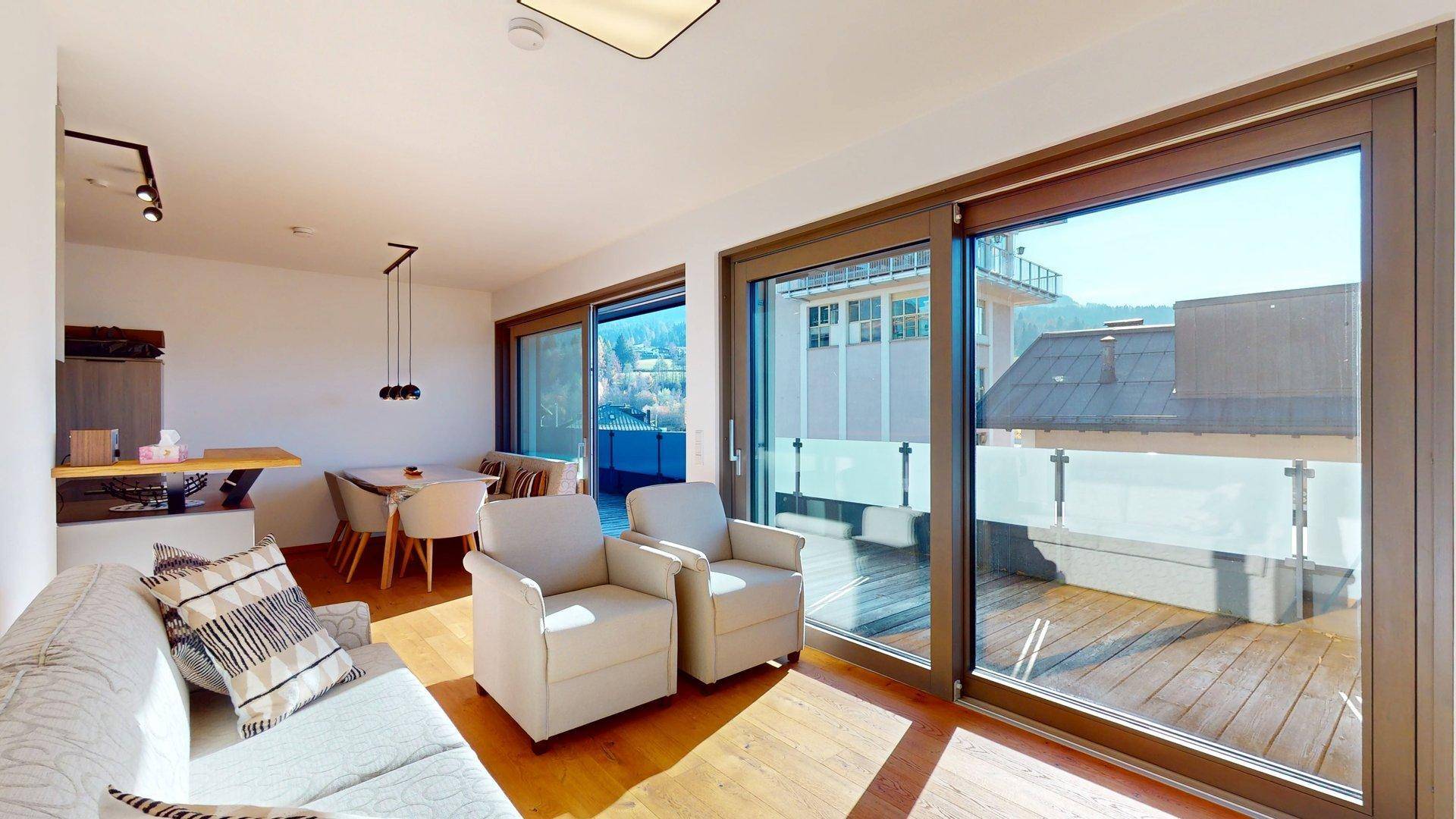 Gemütlicher Wohnbereich mit bequemen Sesseln, Holzboden und großen Schiebetüren zur Terrasse.