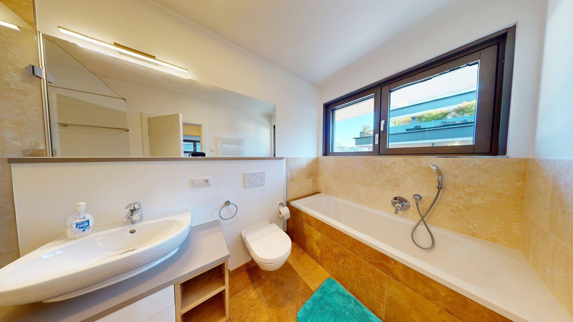 Badezimmer mit Badewanne, Einzelwaschbecken, Toilette und Fenster für natürliches Licht.