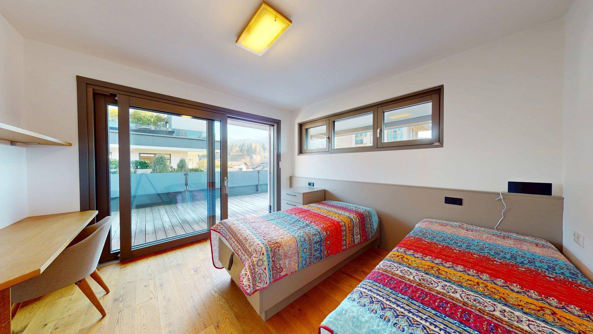 Helles Schlafzimmer mit zwei Einzelbetten, Schreibtisch und direktem Zugang zur Terrasse.