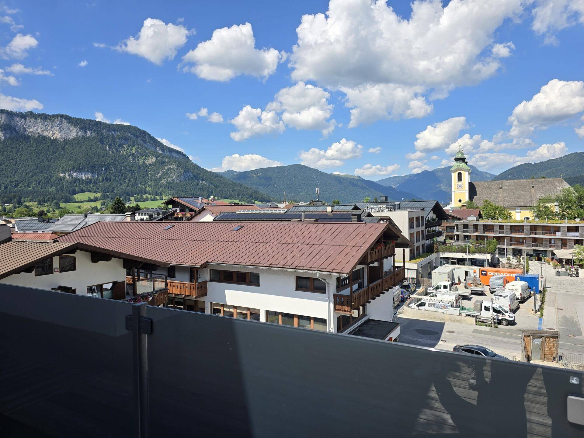 Terrasse mit weitem Blick über die Stadt, inklusive Kirchturm, und die umliegende Berglandschaft.