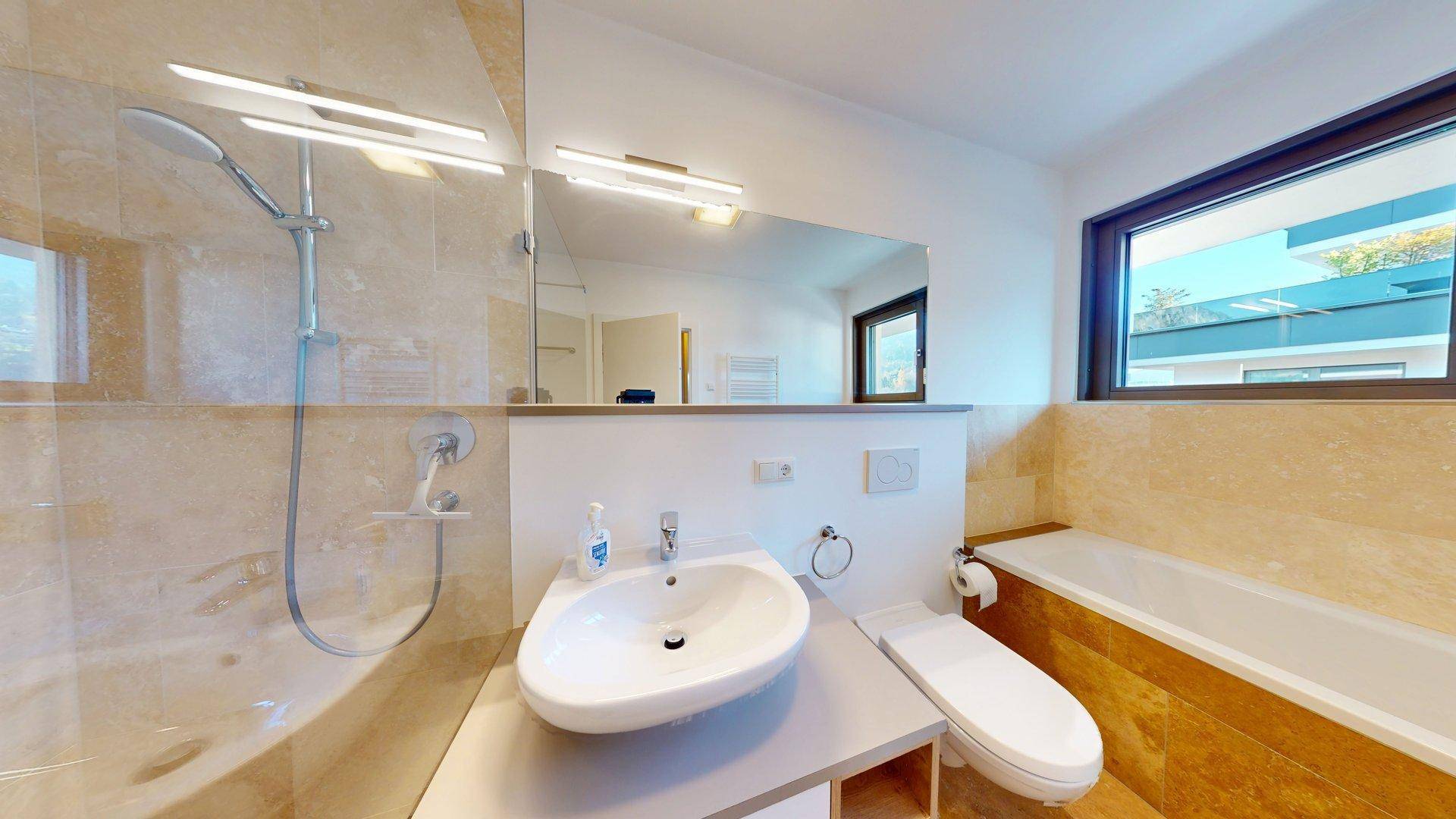Modernes Badezimmer mit Duschbereich, Einzelwaschbecken und Toilette, hell gefliest.