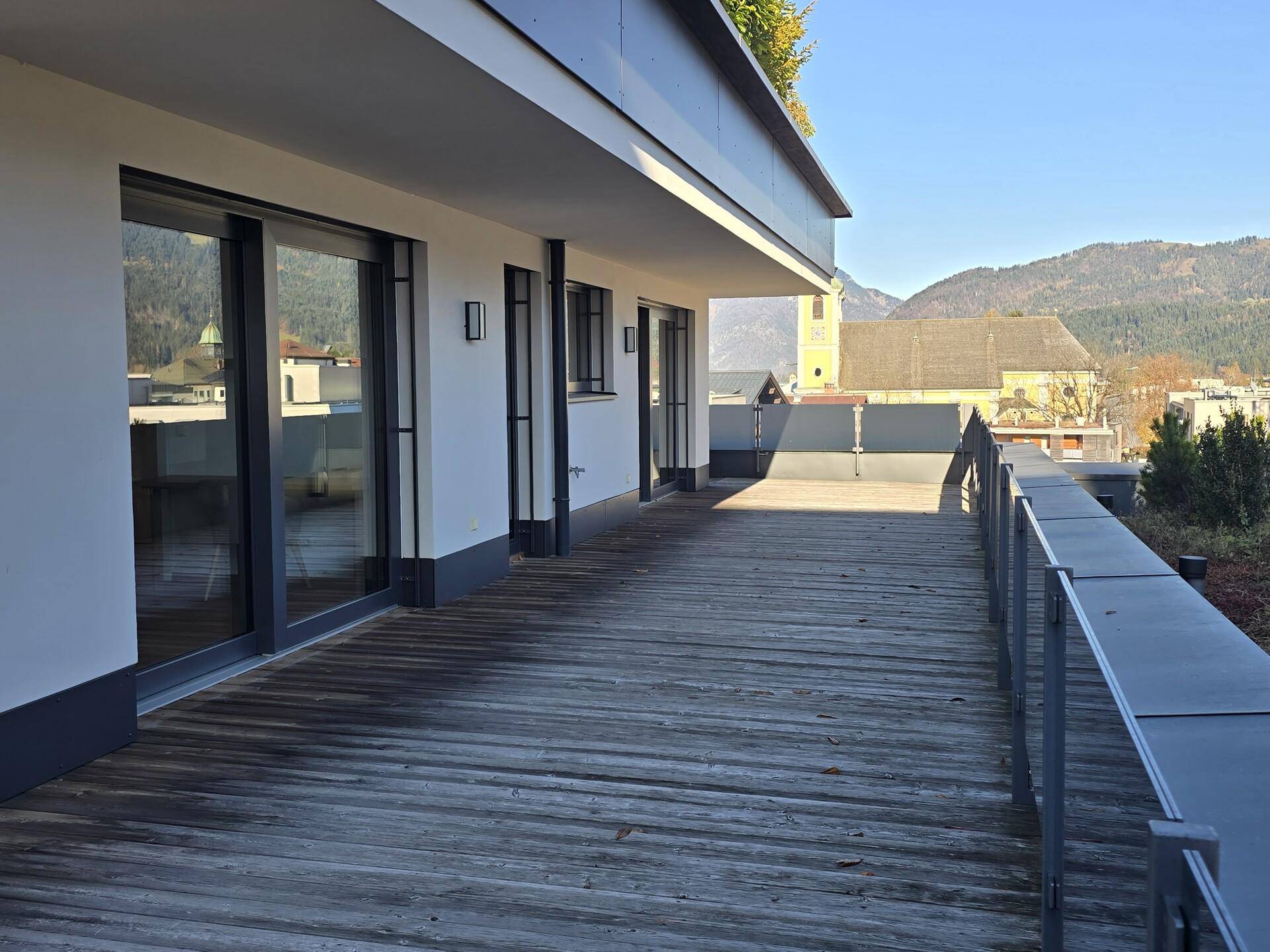 Lange Terrasse mit Holzboden und großen Schiebetüren, die den Zugang zum Innenbereich ermöglichen.