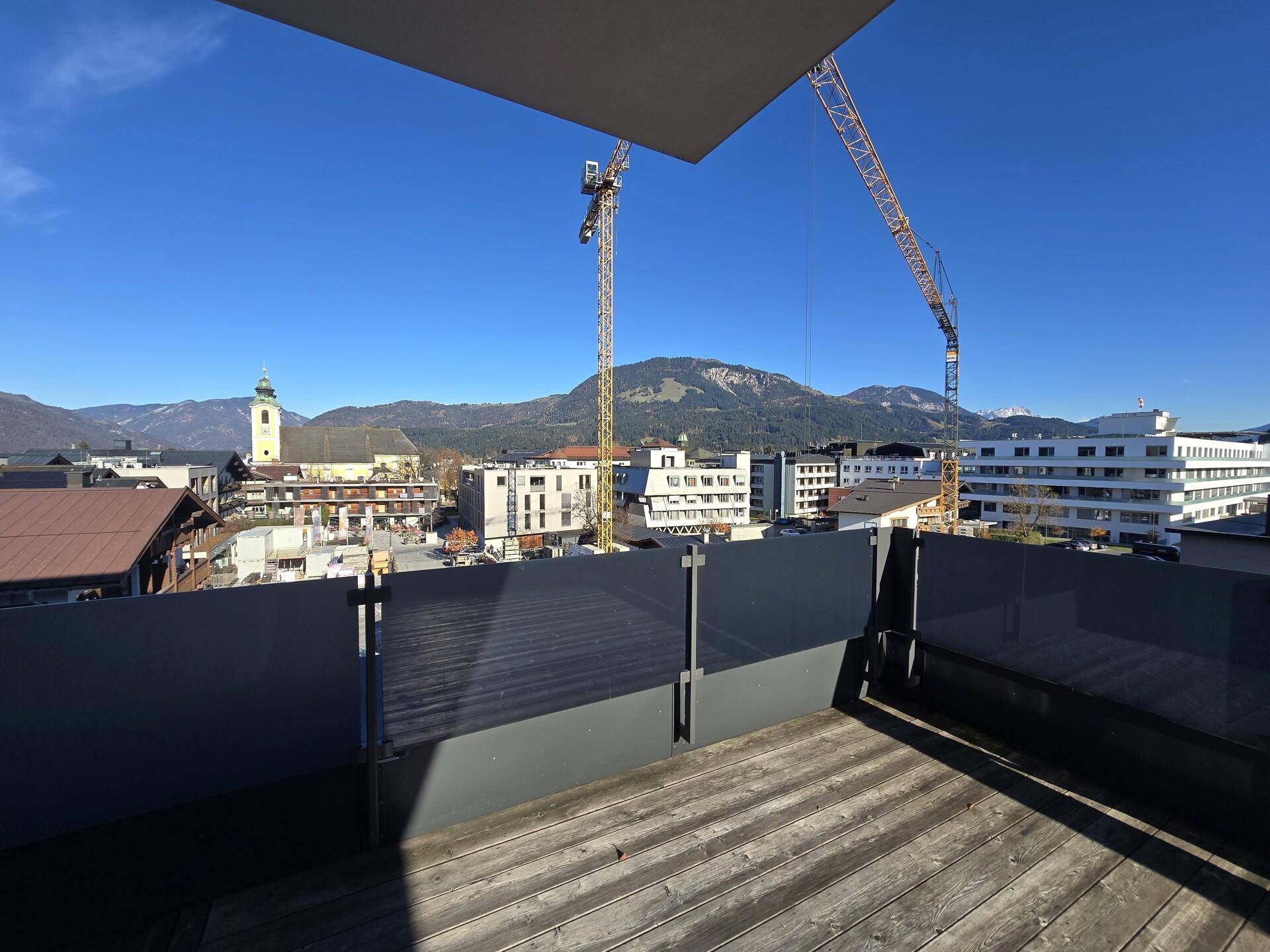 Terrasse mit Blick auf die Stadt, Baustellenkräne und die umliegende Berglandschaft.