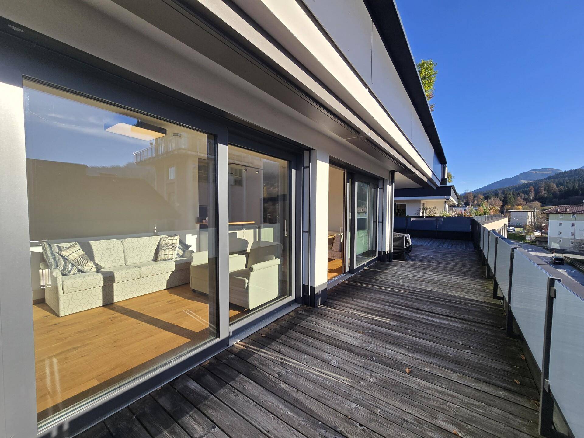 Geräumige Terrasse mit Holzboden und großen Glasfronten, die den Blick ins Wohnzimmer freigeben.