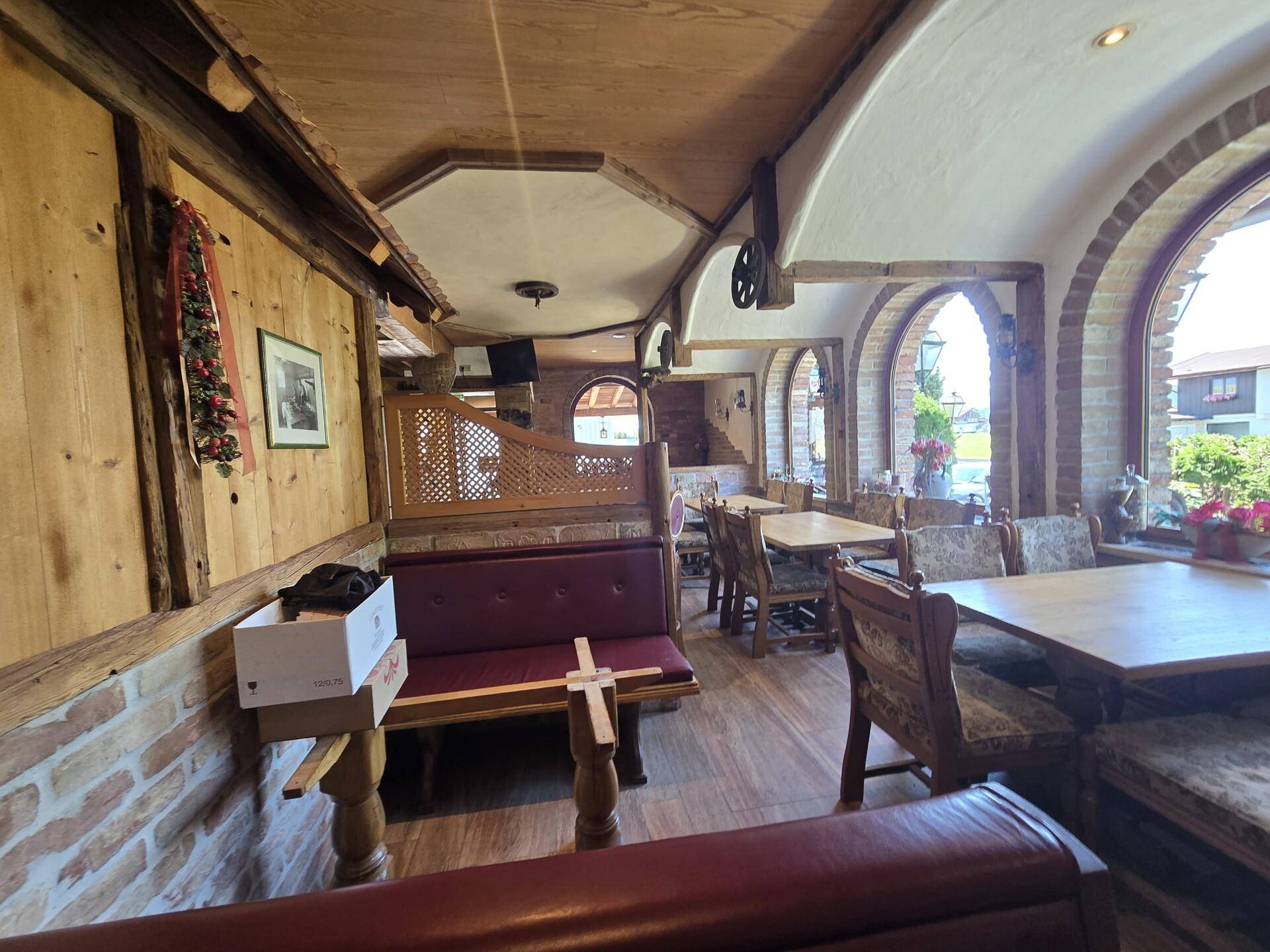 Rustikaler Speisesaal mit Holzbänken, Tischen und Rundbogenfenstern, die viel natürliches Licht hereinlassen.