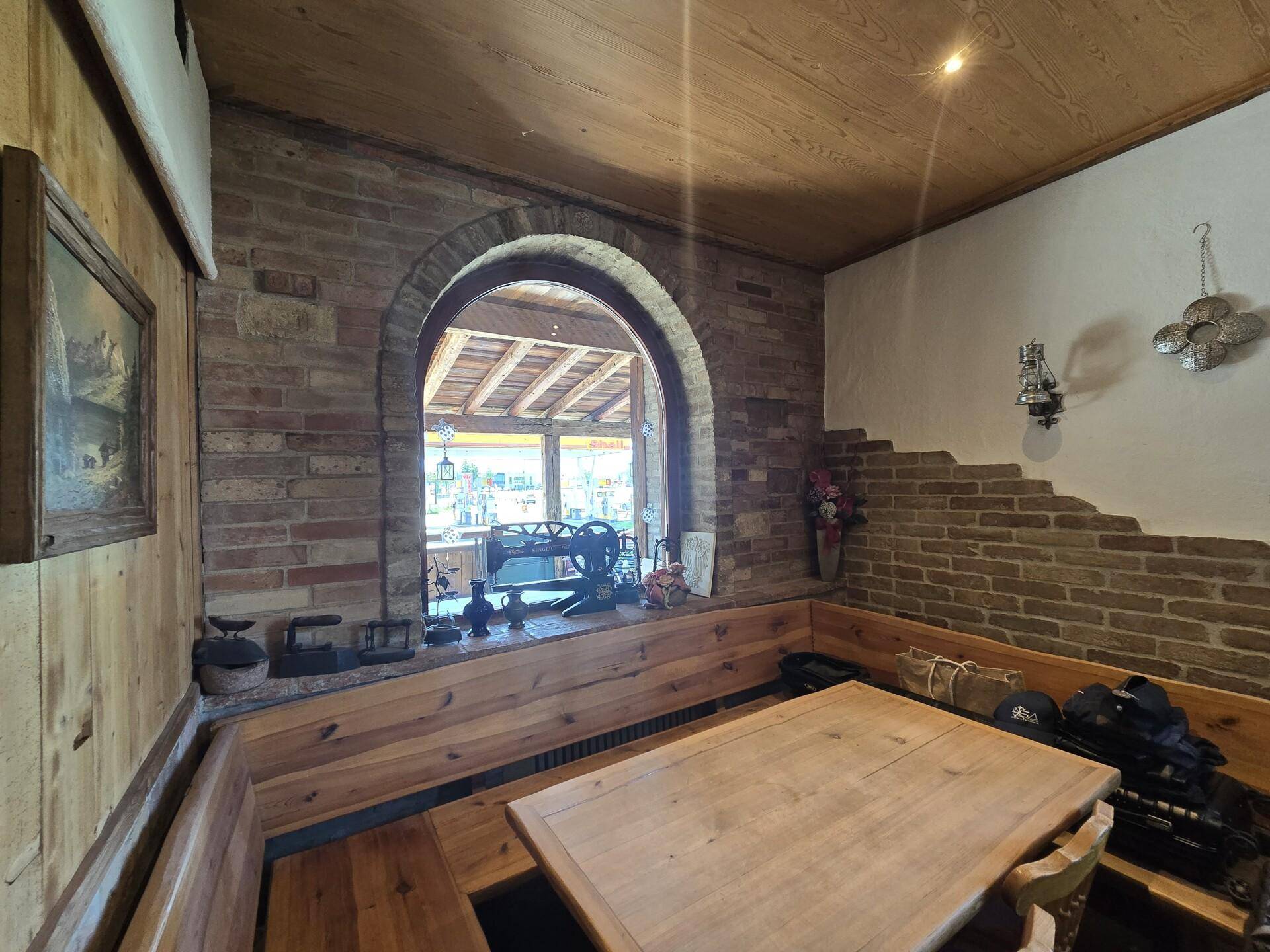 Gemütlicher Essbereich mit Holzbänken und einem Holztisch, umgeben von Ziegelwänden und einem Bogenfenster.