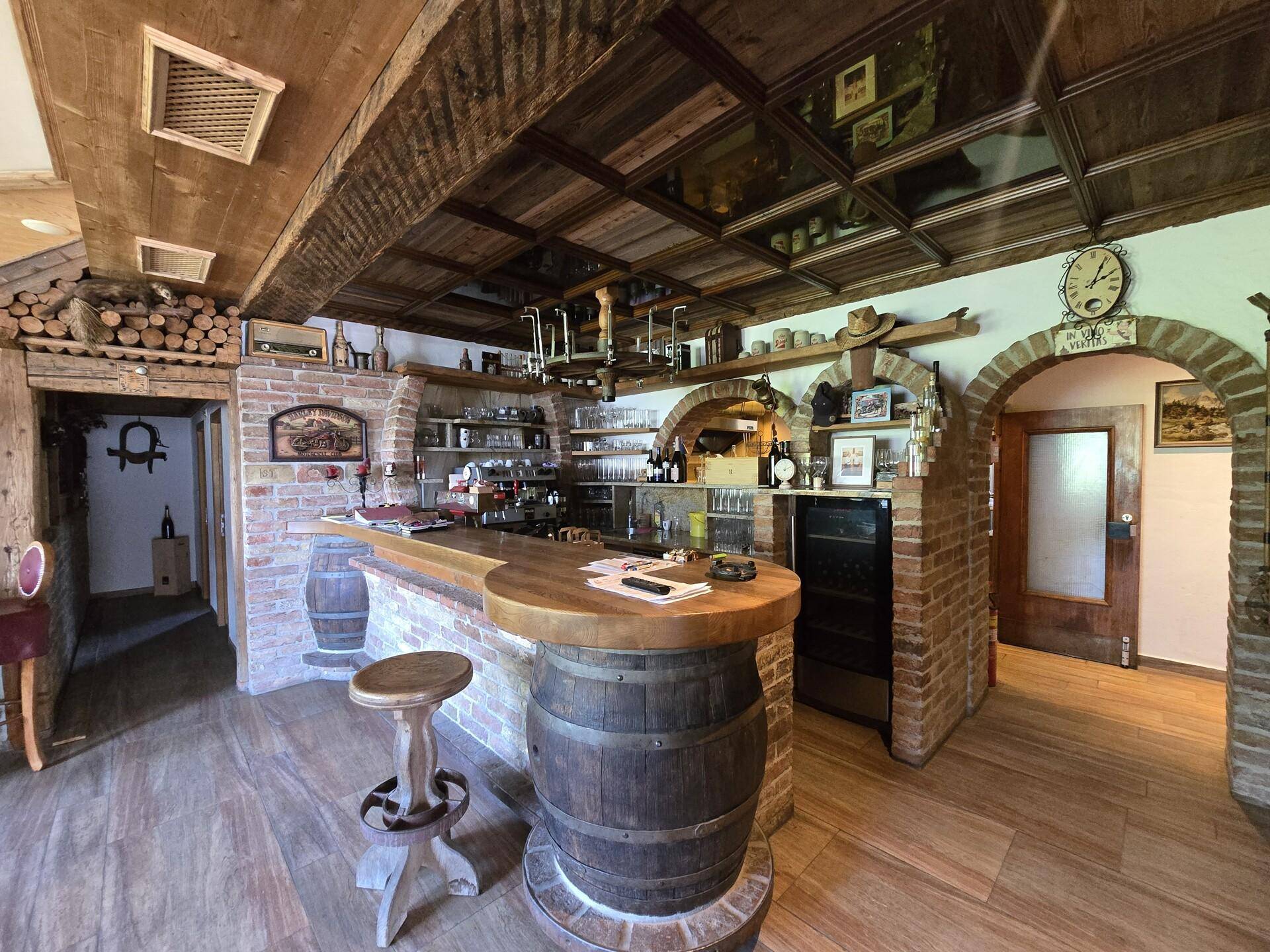 Rustikale Bar mit Holzbalkendecke, Ziegelwänden und einem Tresen aus Holzfässern, ideal für gesellige Abende.