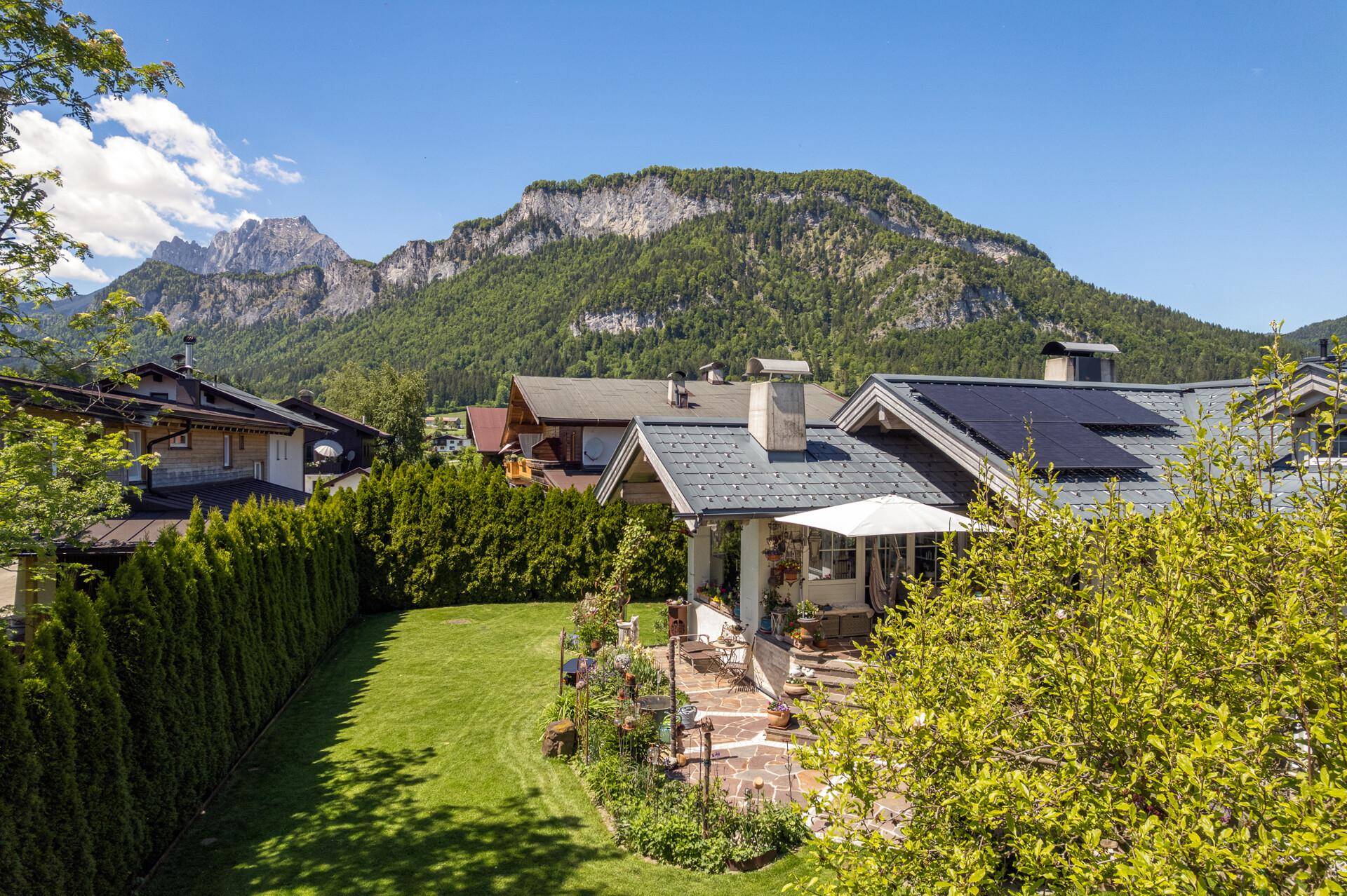 Charmantes Haus mit gepflegtem Garten und Terrasse, umgeben von einer malerischen Berglandschaft.