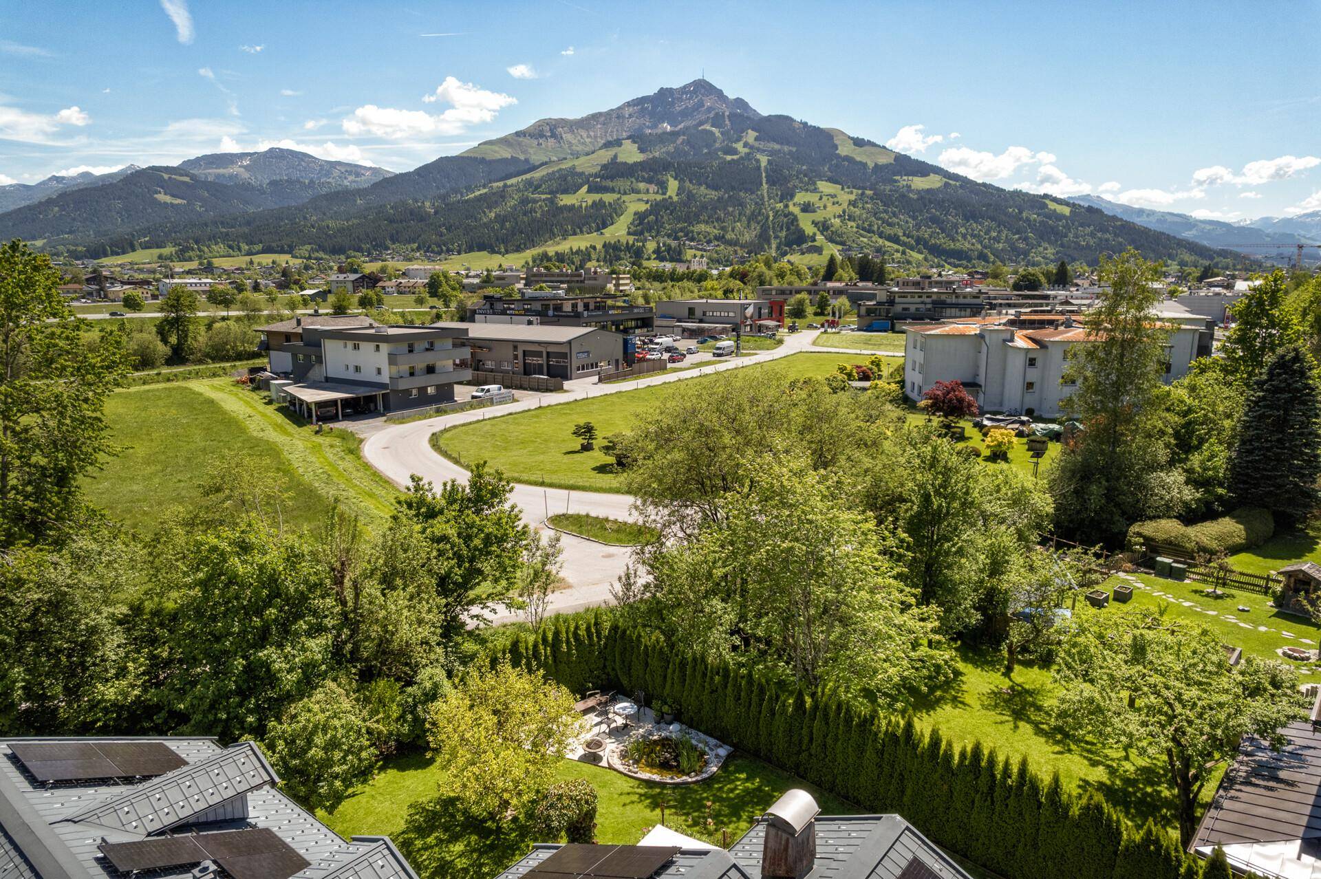 Weitläufige Luftaufnahme der Umgebung mit Wohngebiet, grünen Feldern und imposanten Bergen.