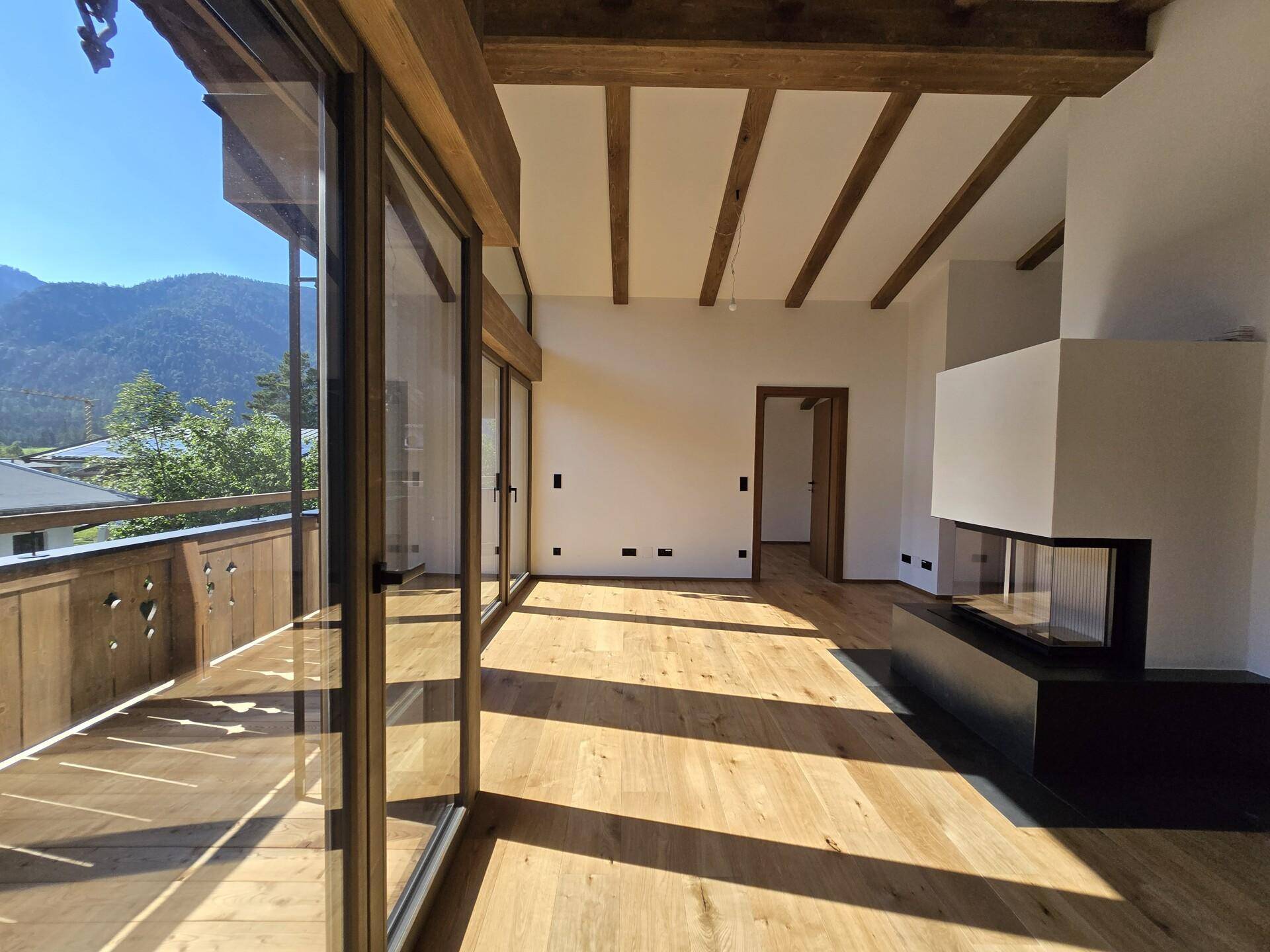 Helles Wohnzimmer mit Holzbalkendecke, Eichenparkett und großflächigen Fenstern mit Bergblick.