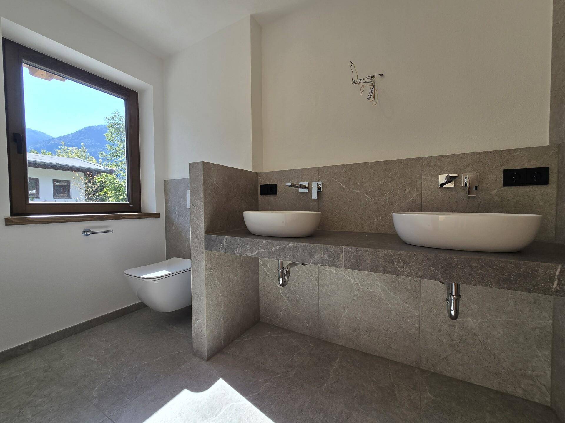 Modernes Badezimmer mit Doppelwaschbecken, Wand-WC und großem Fenster mit Bergblick.