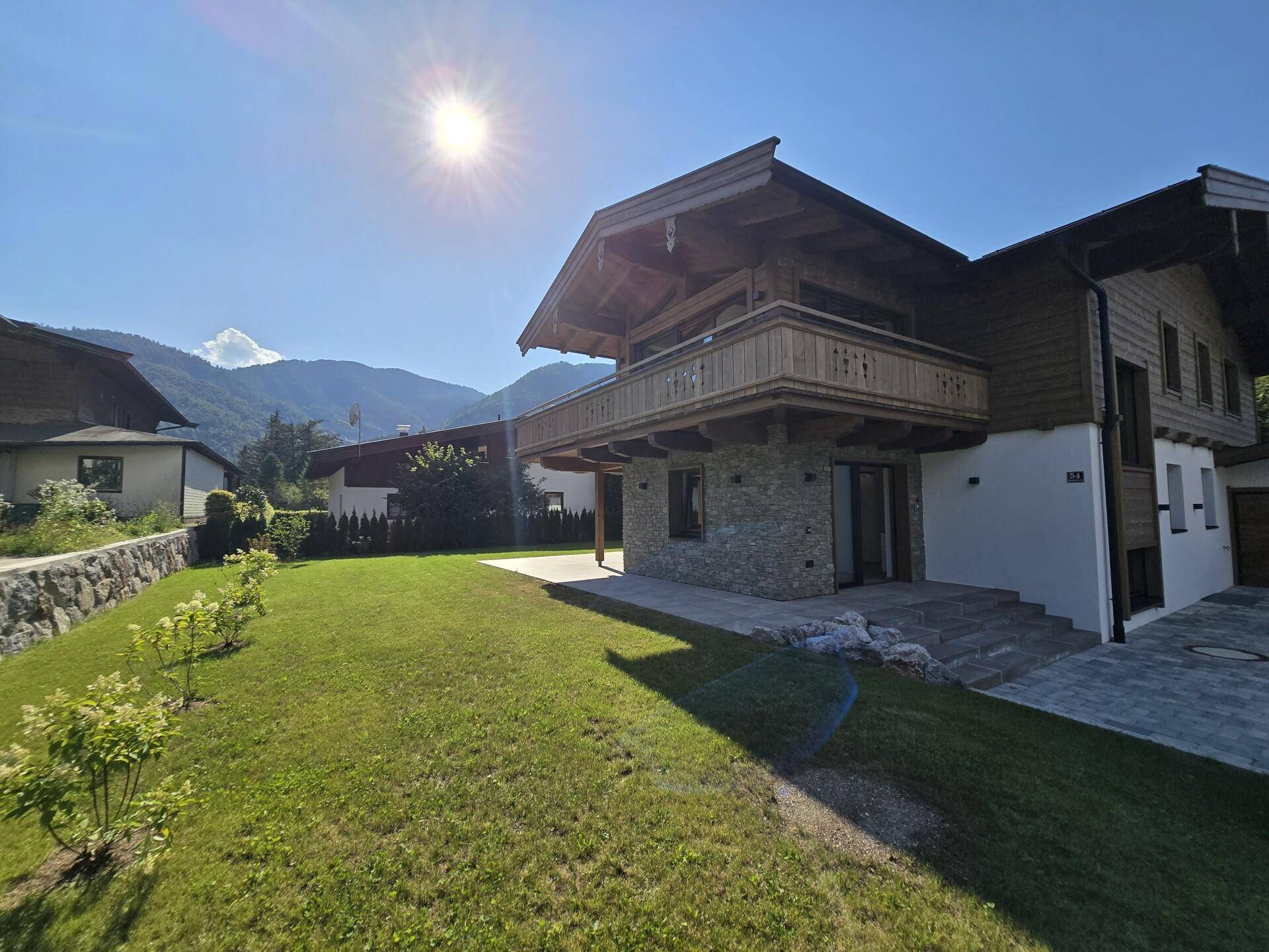 Sonniges Chalet mit gepflegtem Vorgarten und Bergblick unter blauem Himmel.