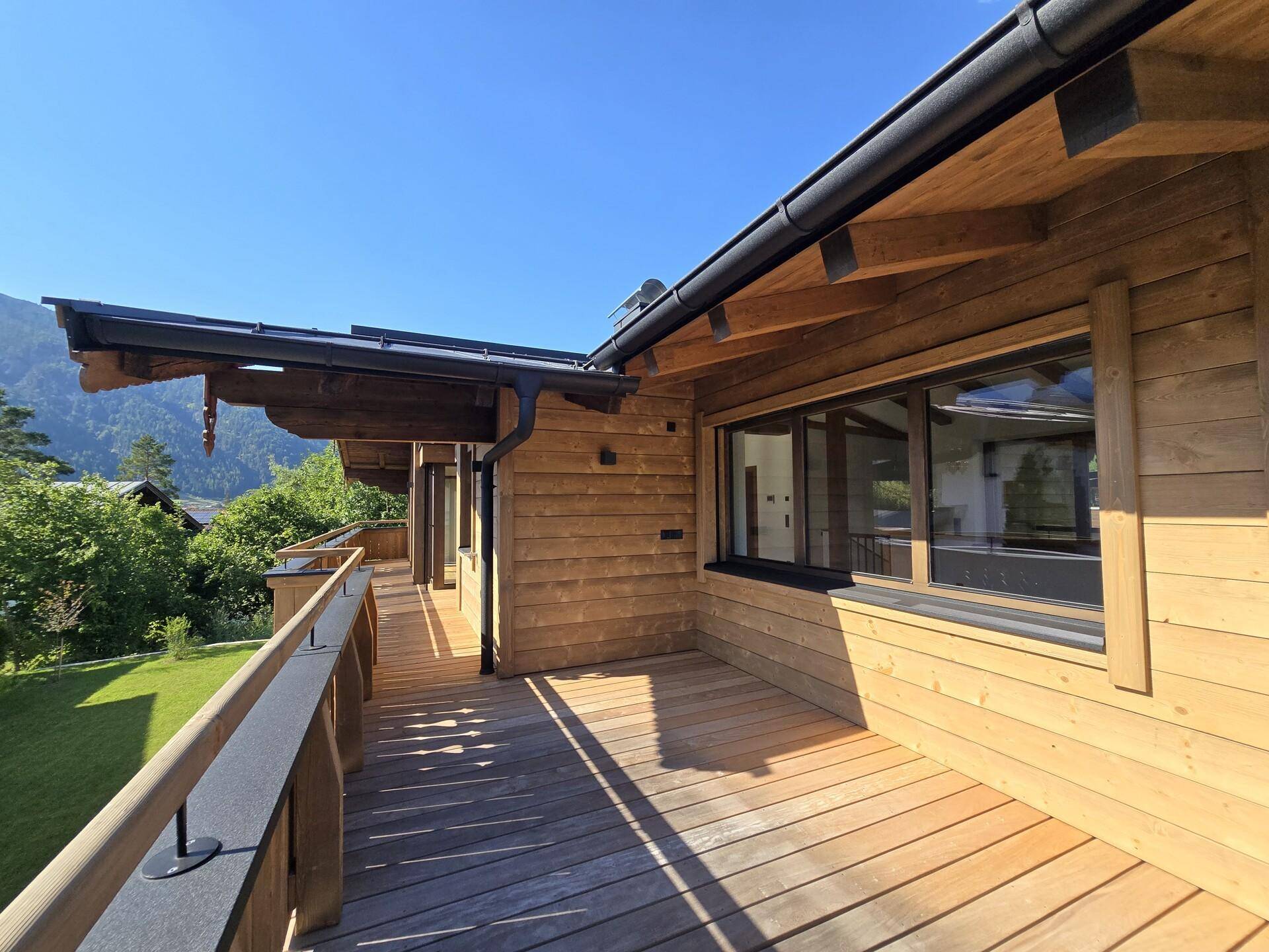 Langer Holzbalkon mit traditionellem Geländer und Blick auf die umliegende Berglandschaft.