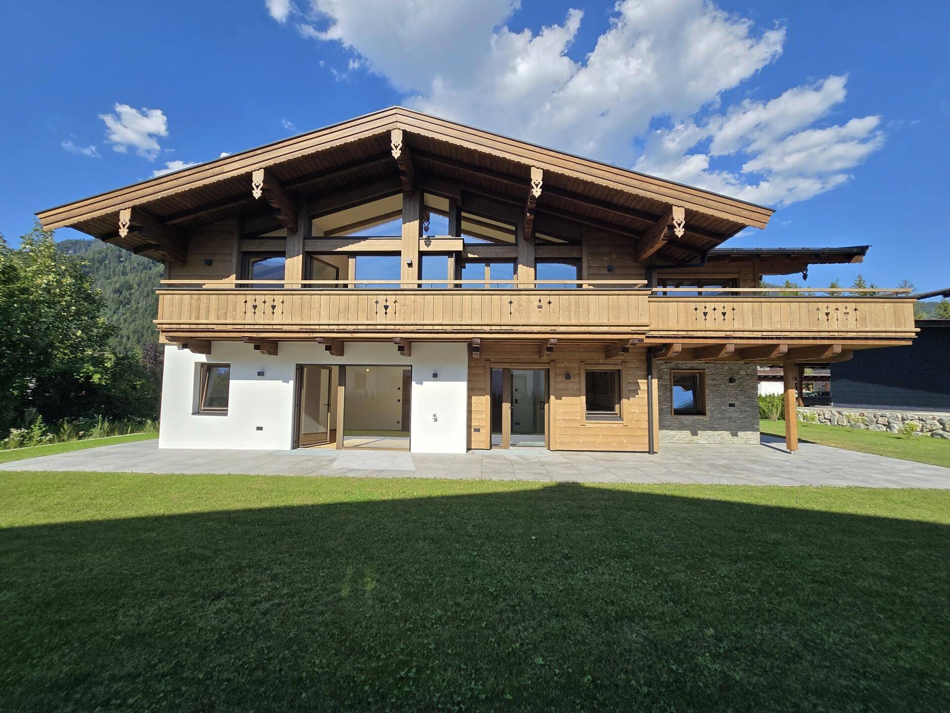 Frontansicht eines modernen Chalets mit Holzfassade, großen Fenstern und Balkonen.