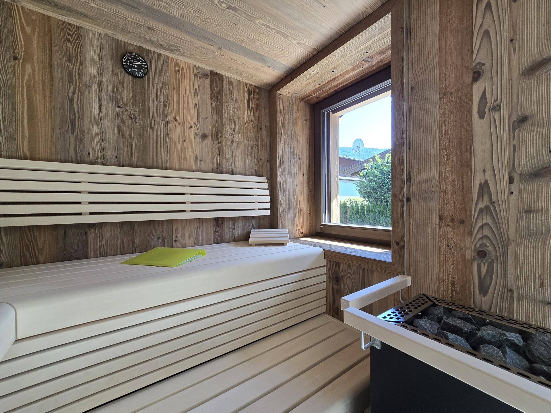 Moderne Holzsauna mit breiten Bänken und einem Fenster, das Tageslicht hereinlässt.