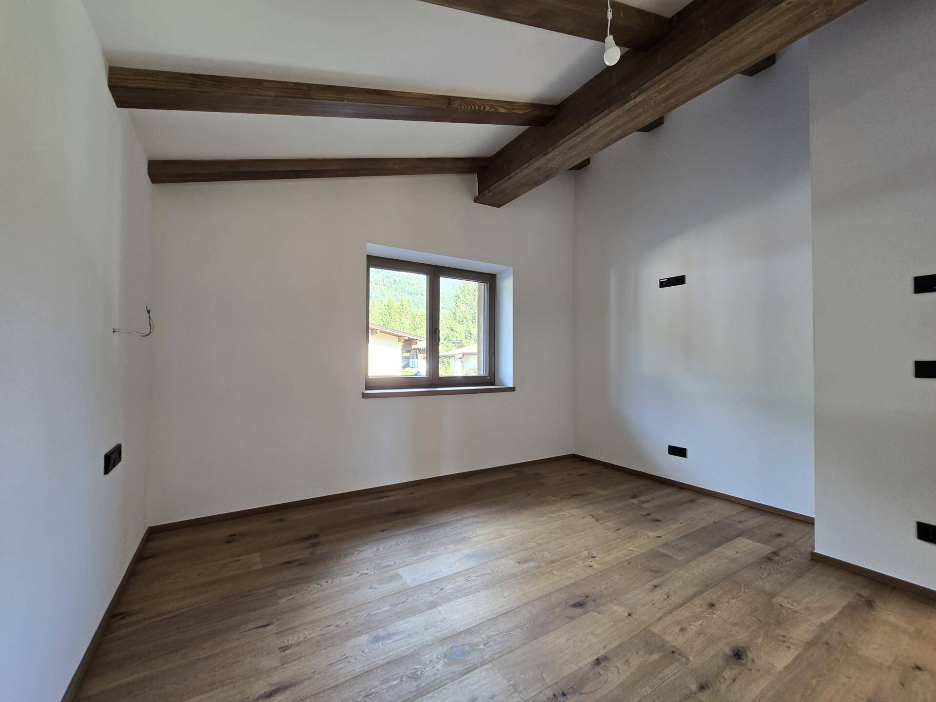 Geräumiges Schlafzimmer mit Eichenparkett und einem Fenster, das viel Tageslicht hereinlässt.