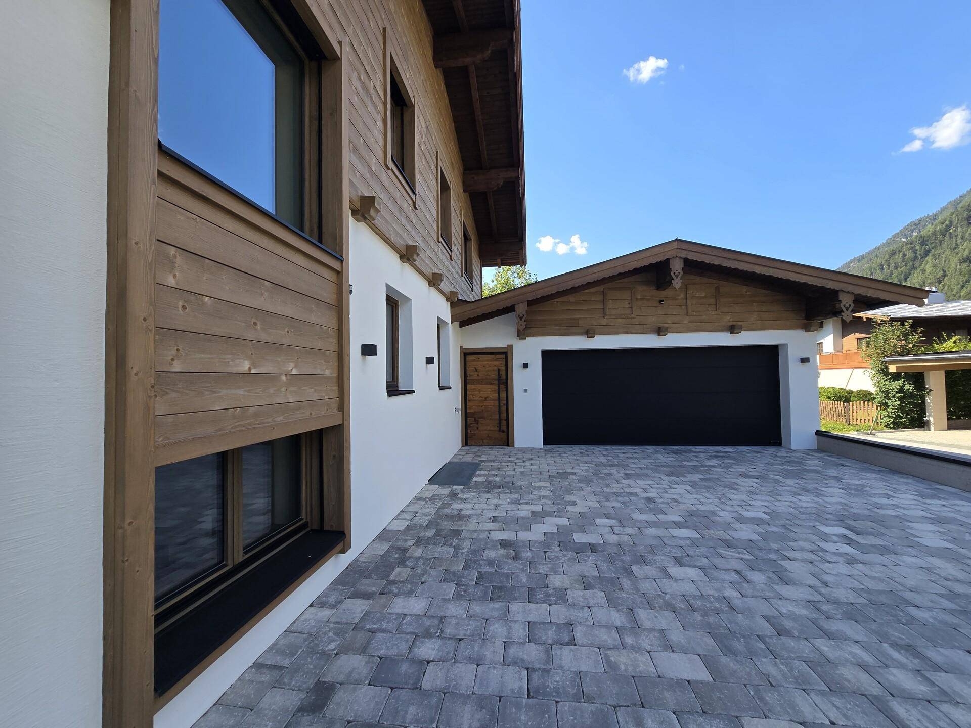 Geräumige Doppelgarage mit schwarzem Tor und gepflasterter Zufahrt zum modernen Chalet.