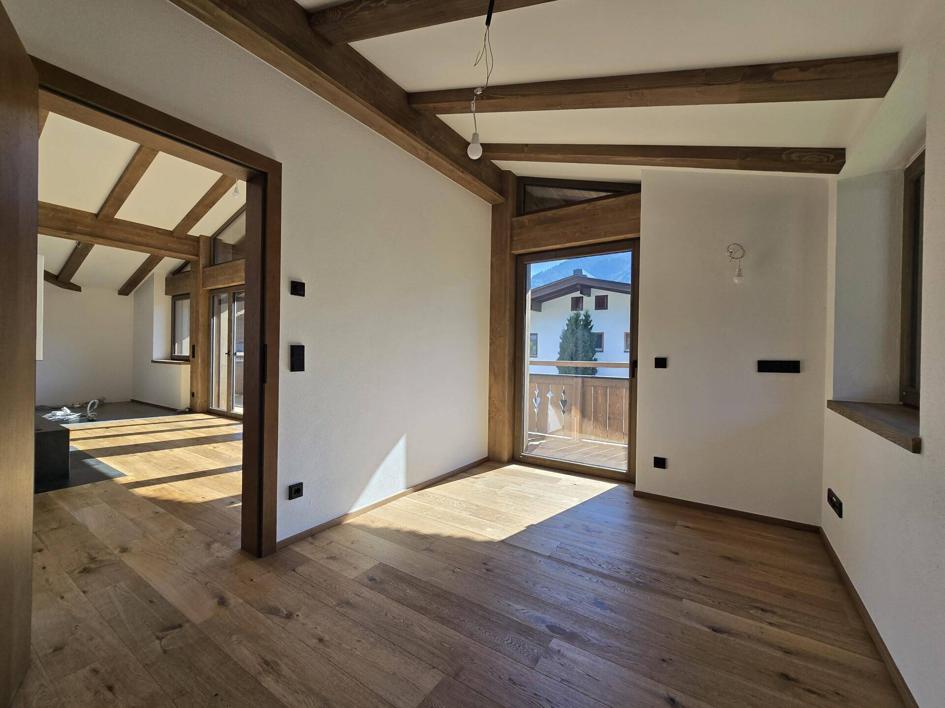 Helles Zimmer mit Eichenparkett, Holzbalken und Zugang zu einem Balkon.