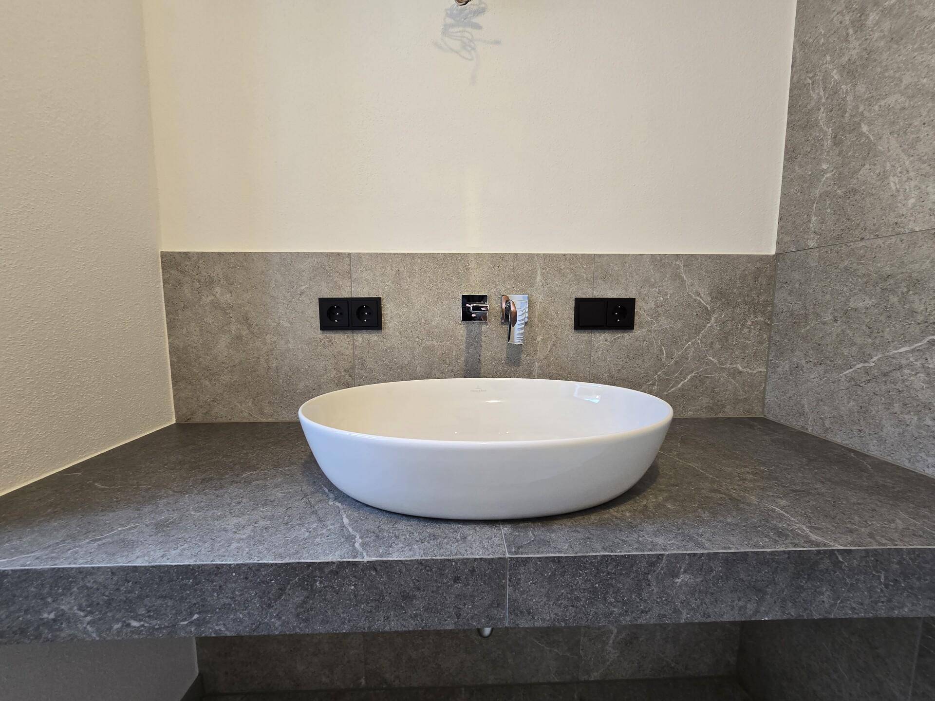 Modernes Einzelwaschbecken auf einer grauen Ablagefläche mit minimalistischen Armaturen.
