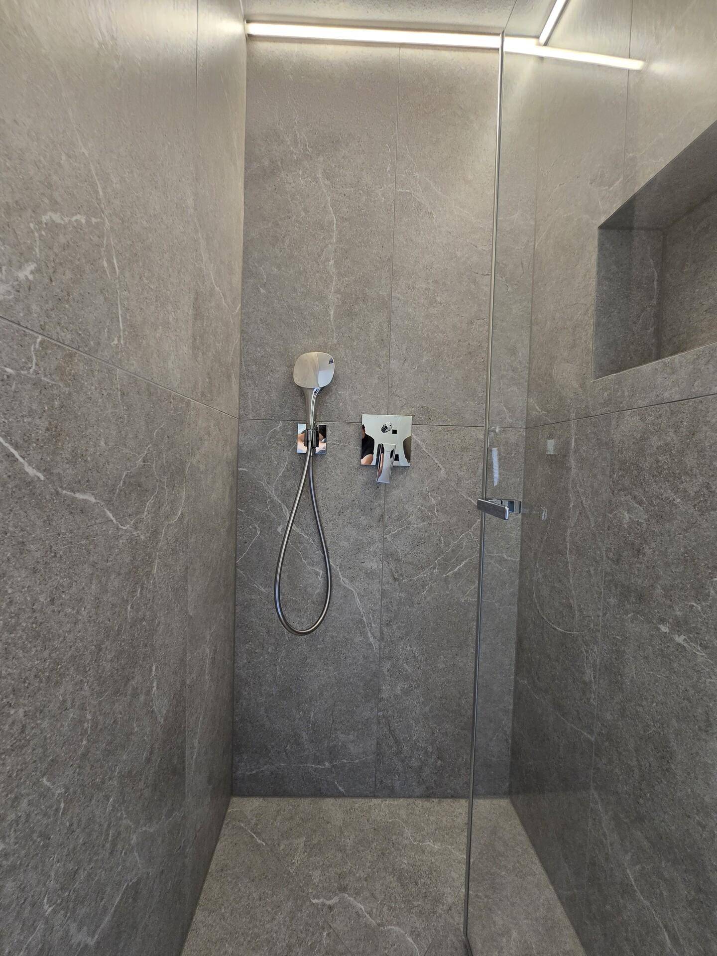 Ebenerdige Dusche mit modernen grauen Fliesen und integrierter Beleuchtung.