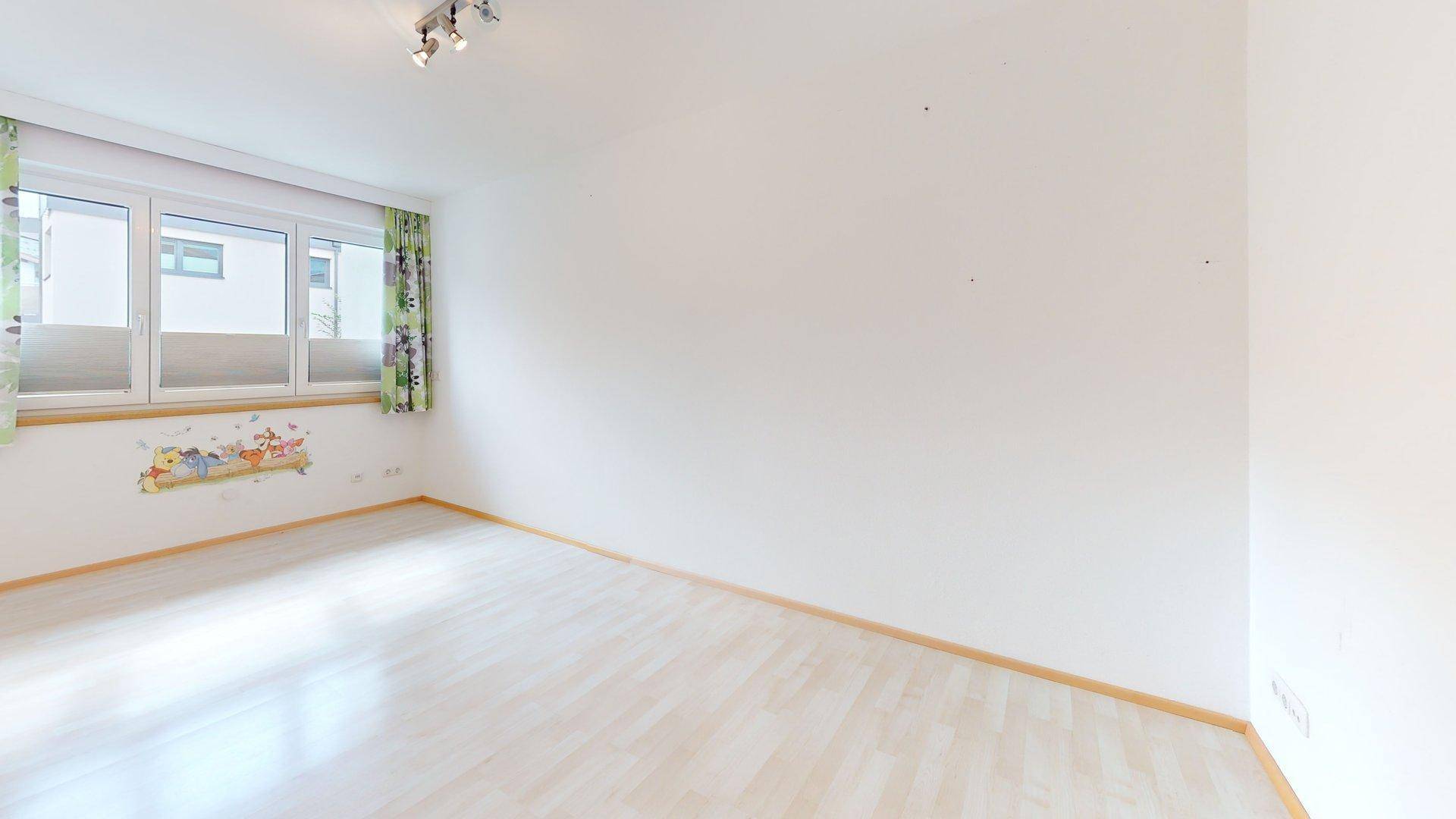 Helles, leeres Zimmer mit Laminatboden und Fenster, bereit zur individuellen Gestaltung.