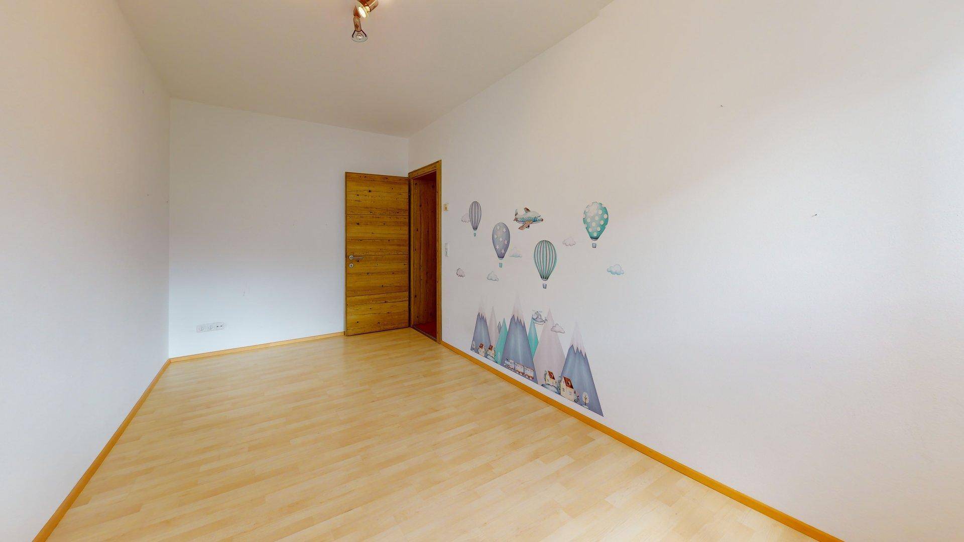 Leeres Zimmer mit hellem Laminatboden und verspielten Wandstickern, ideal als Kinderzimmer.