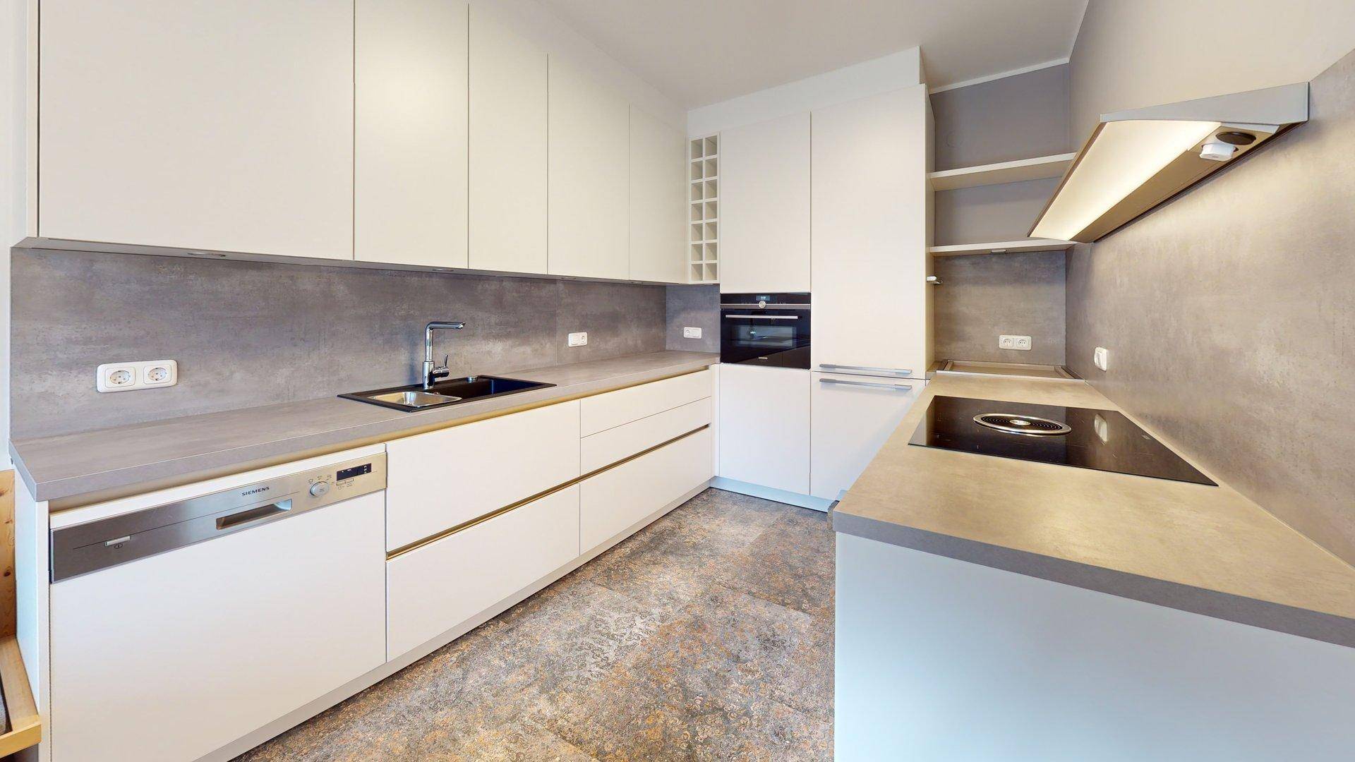 Moderne weiße Einbauküche mit integrierten Geräten, Induktionskochfeld und grauen Arbeitsplatten.