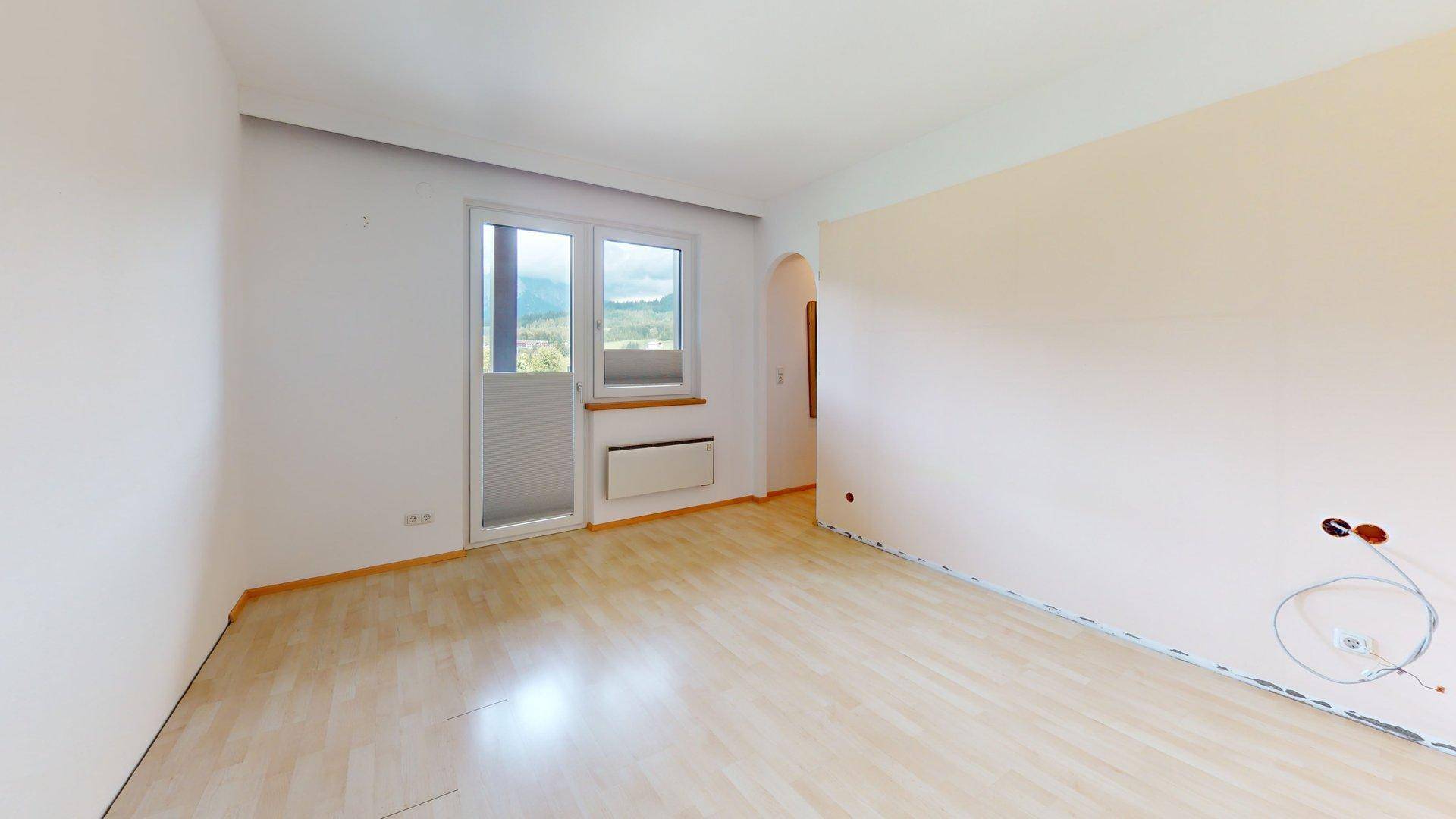 Geräumiges Zimmer mit Laminatboden, Balkonzugang und Blick auf die umliegende Berglandschaft.