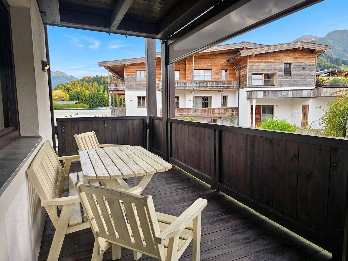 Gemütlicher Holzbalkon mit Sitzgelegenheiten und Blick auf die umliegenden Gebäude und Berge.