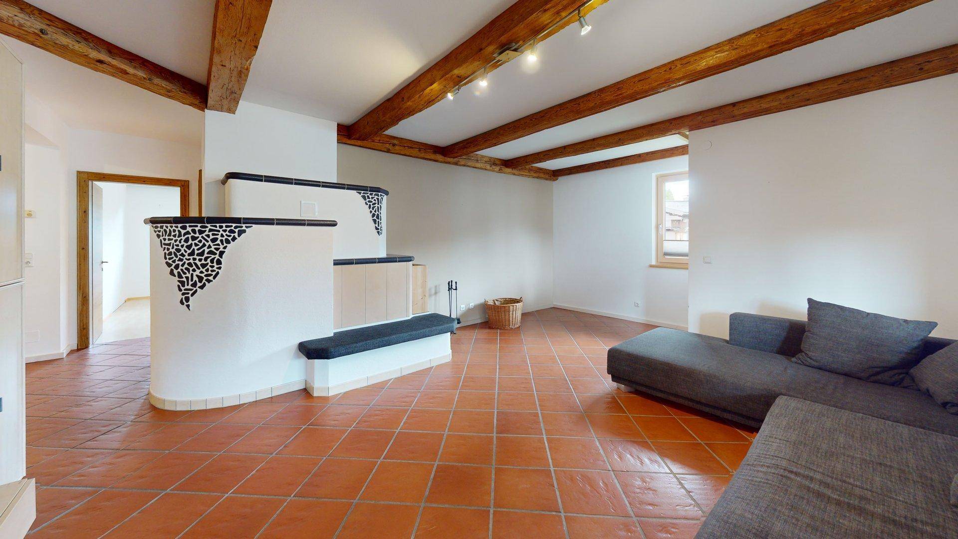 Gemütliches Wohnzimmer mit sichtbaren Holzbalken, Terrakottafliesen und einem dekorativen Kachelofen.