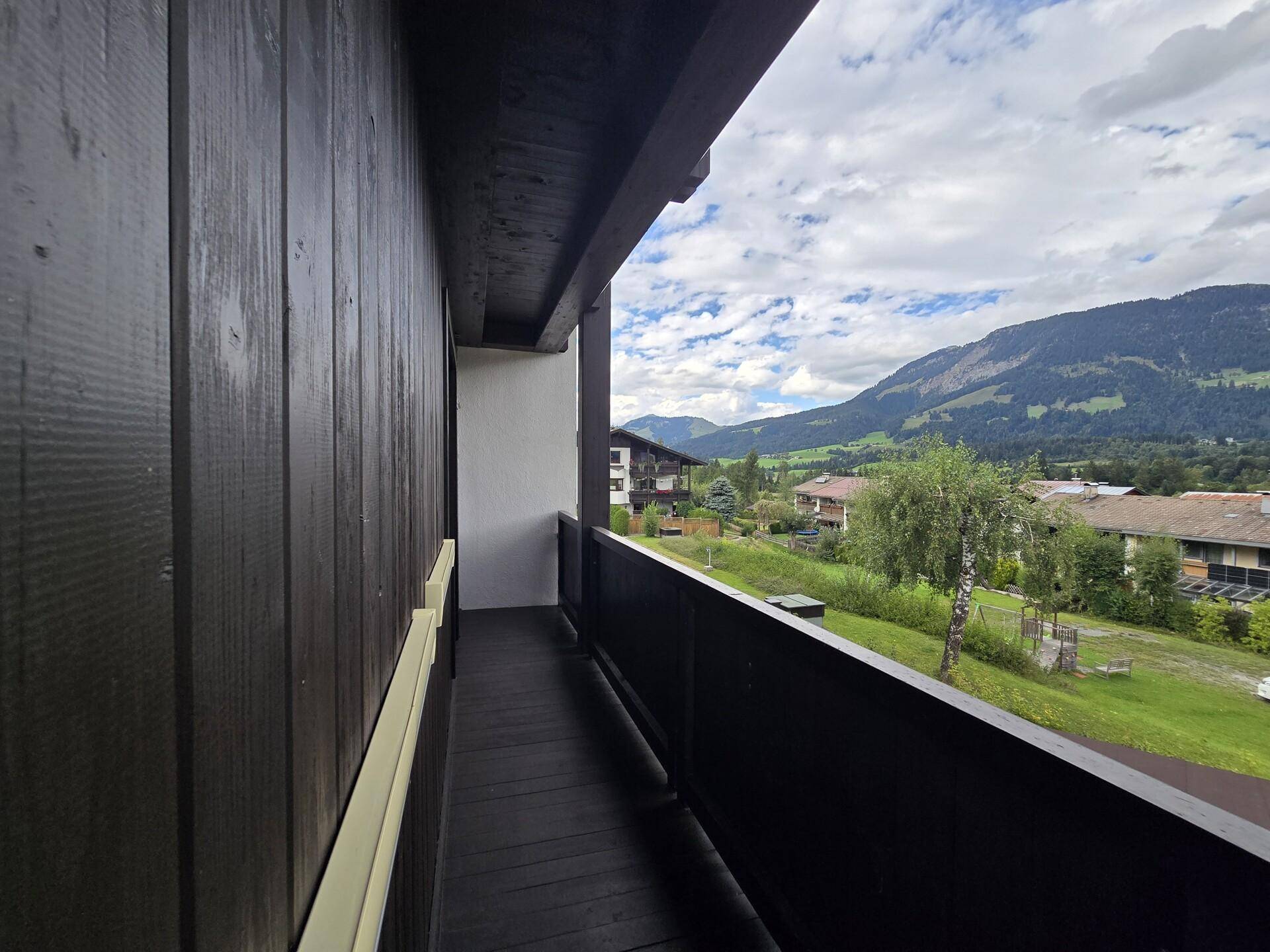 Schmaler Holzbalkon mit Bergblick und grüner Umgebung, ideal für frische Luft.
