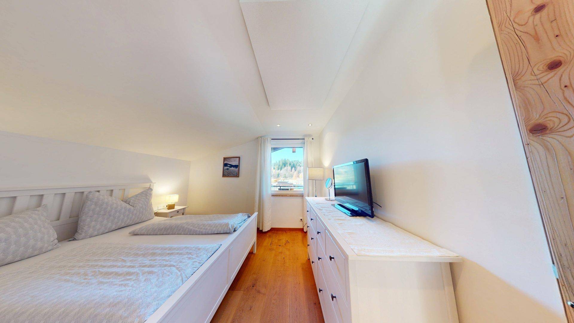 Helles Schlafzimmer mit Doppelbett, Kommode und Dachschräge, bietet einen schönen Ausblick.