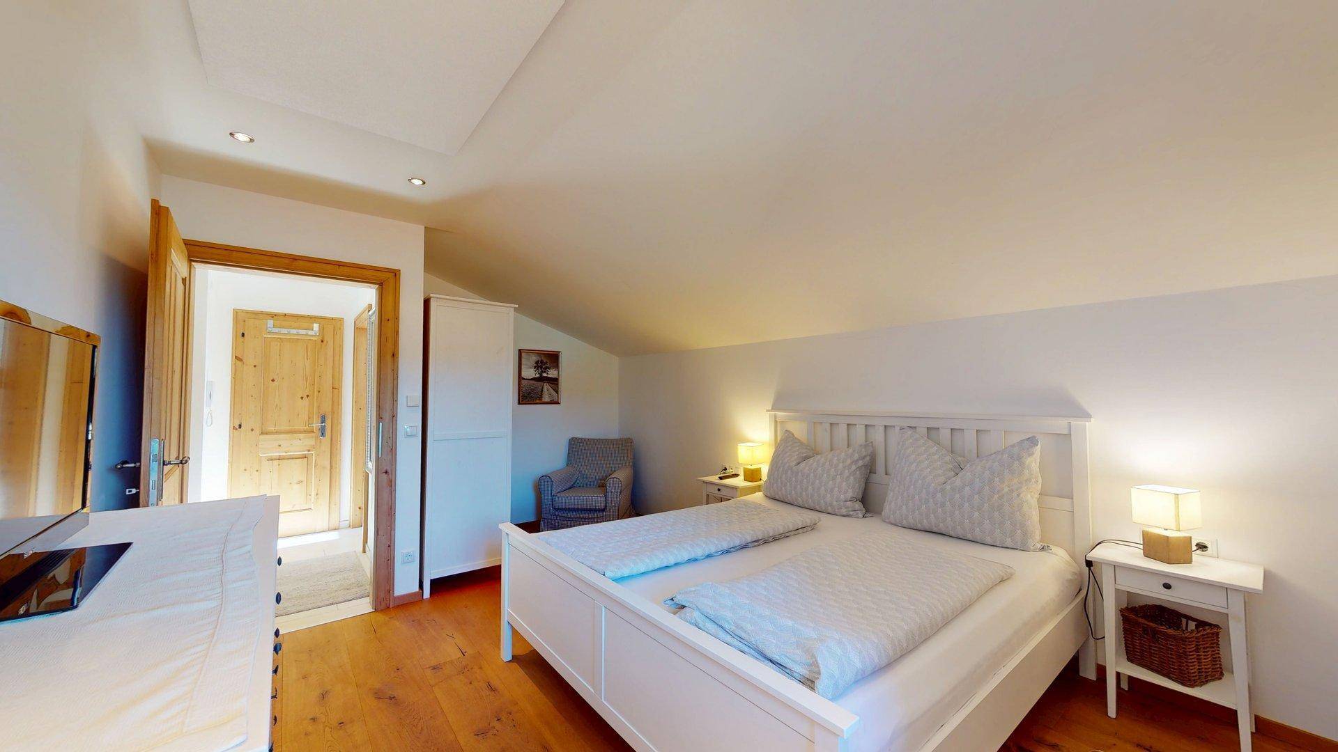 Komfortables Schlafzimmer mit Doppelbett, Kleiderschrank und Holzboden, Zugang zu weiterem Raum.