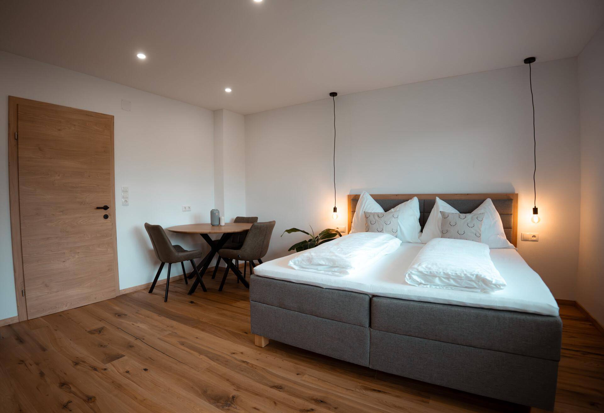 Schlafzimmer mit Holzboden, Doppelbett, Esstisch und einer modernen Holztür.