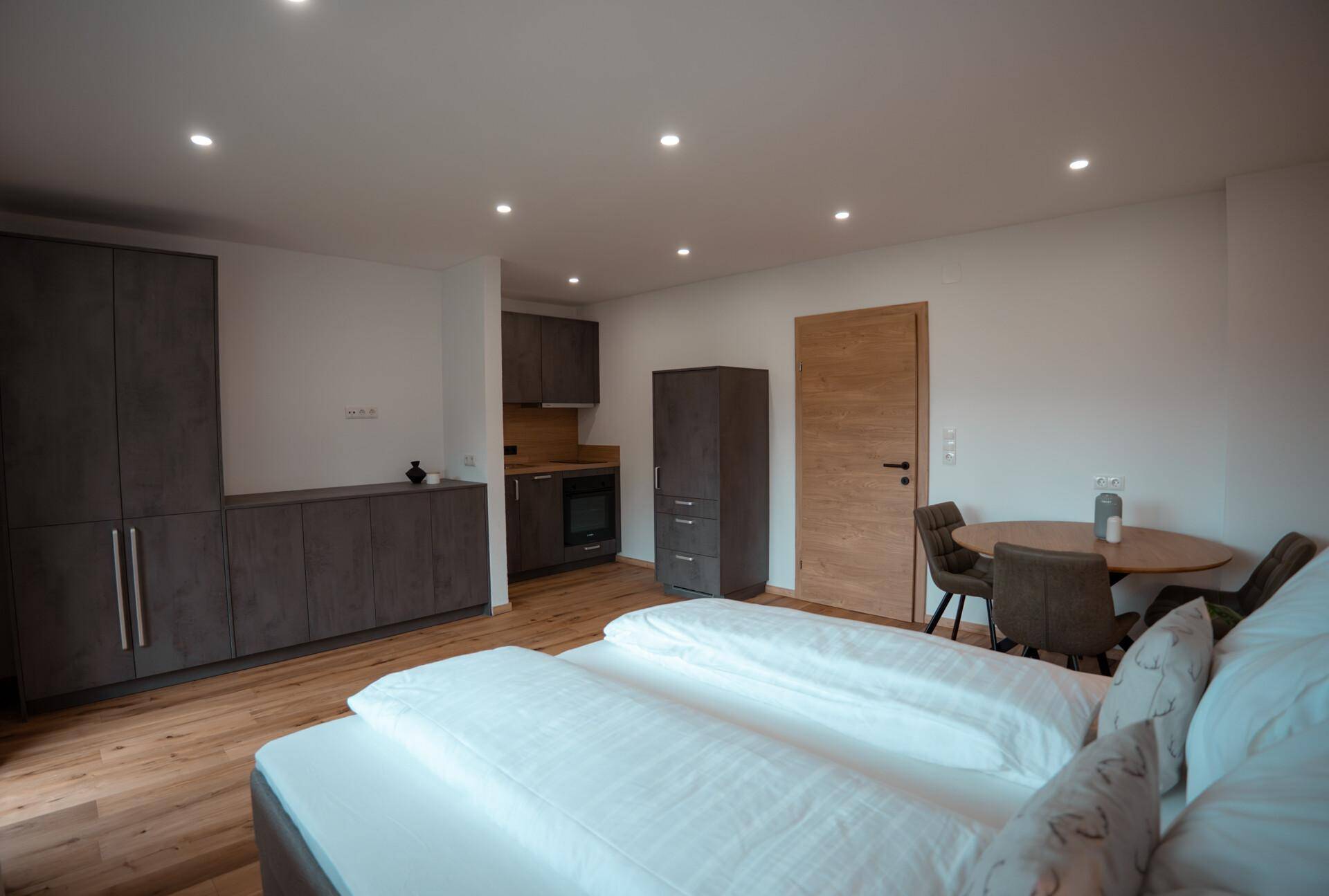 Modernes Schlafzimmer mit integrierter Küchenzeile, Holzboden und Esstisch.