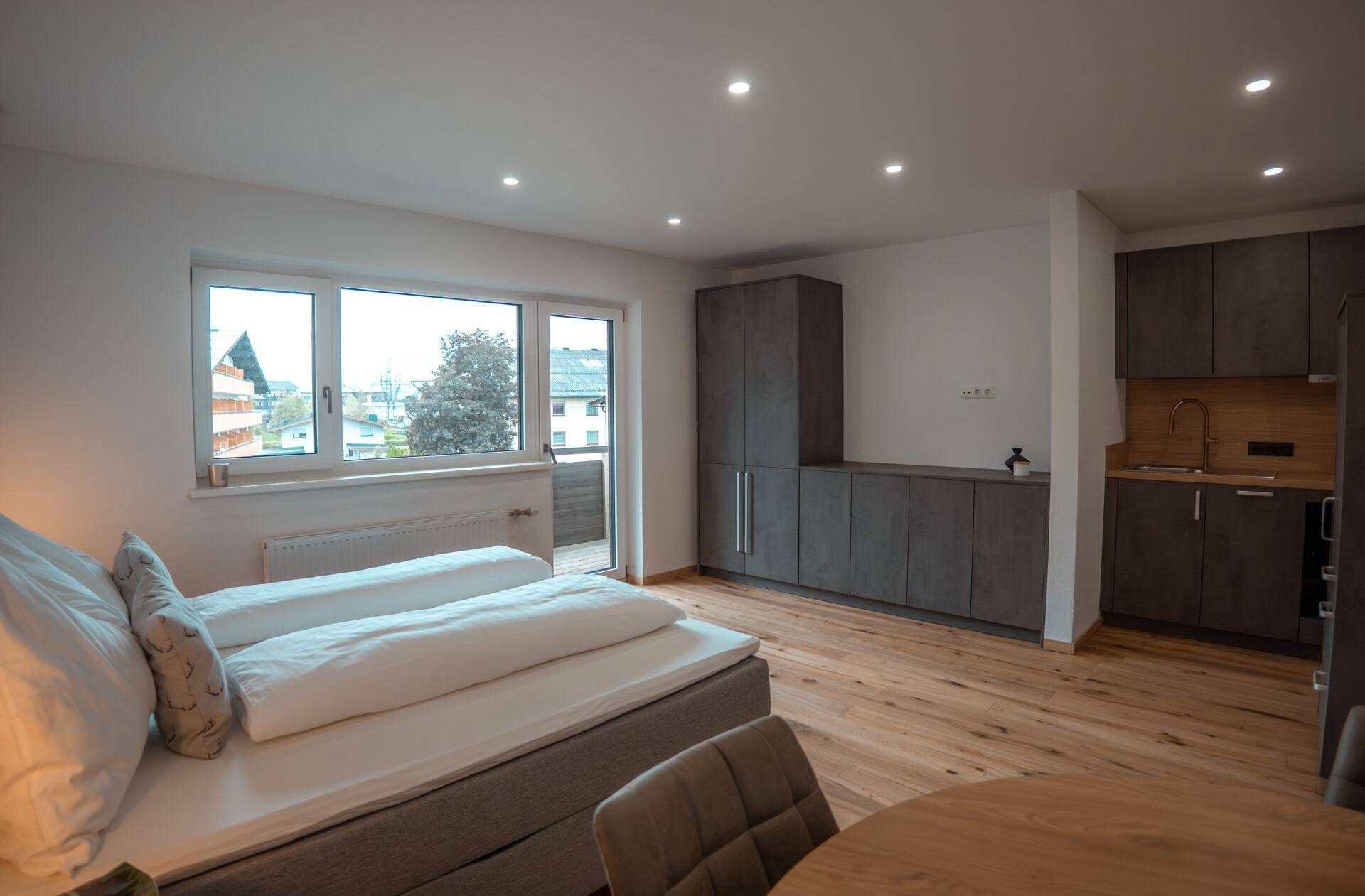 Gemütliches Schlafzimmer mit Küchenzeile, großem Fenster und Zugang zum Balkon.