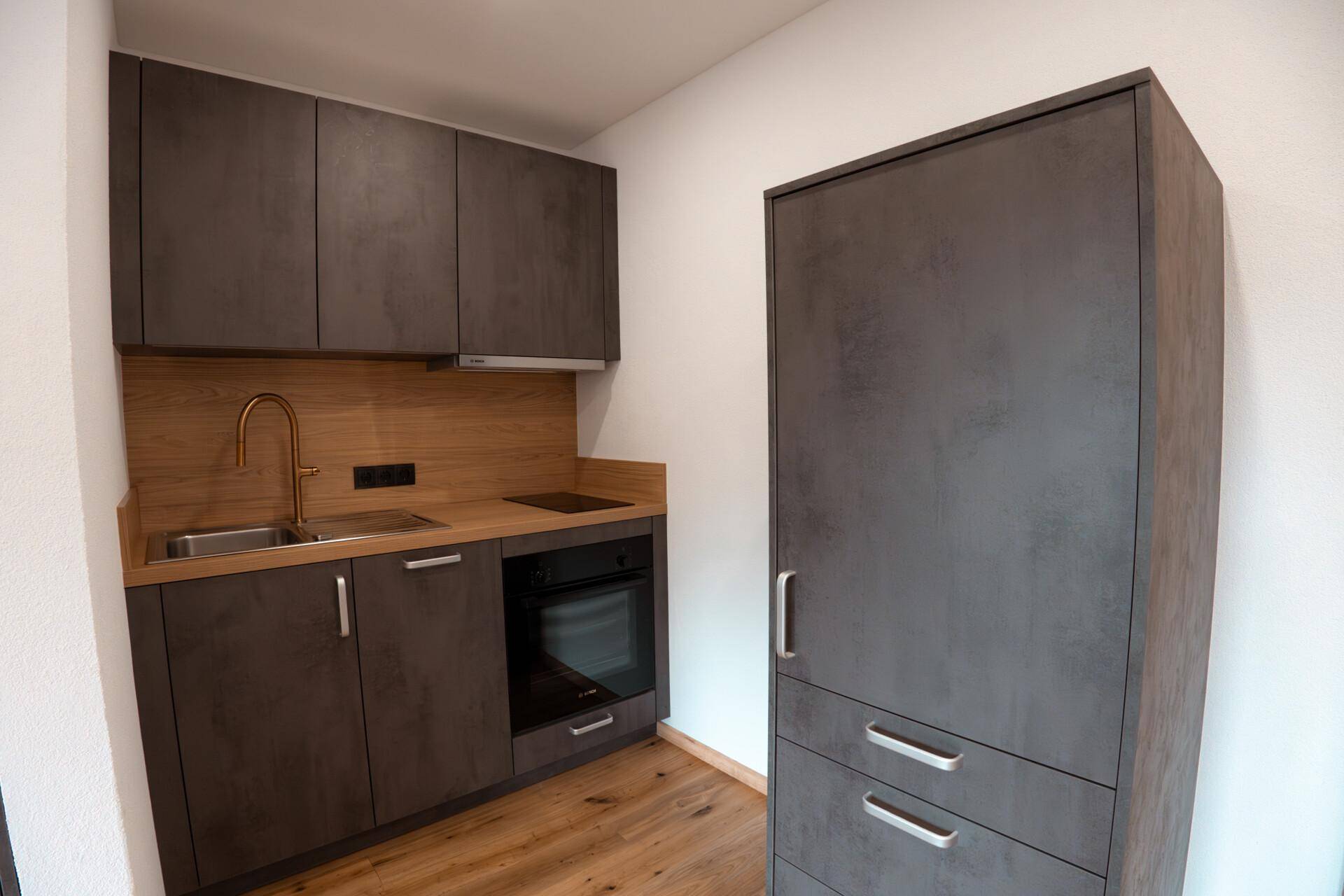 Moderne Küchenzeile mit dunklen Schränken, Holzdetails und integrierten Geräten.