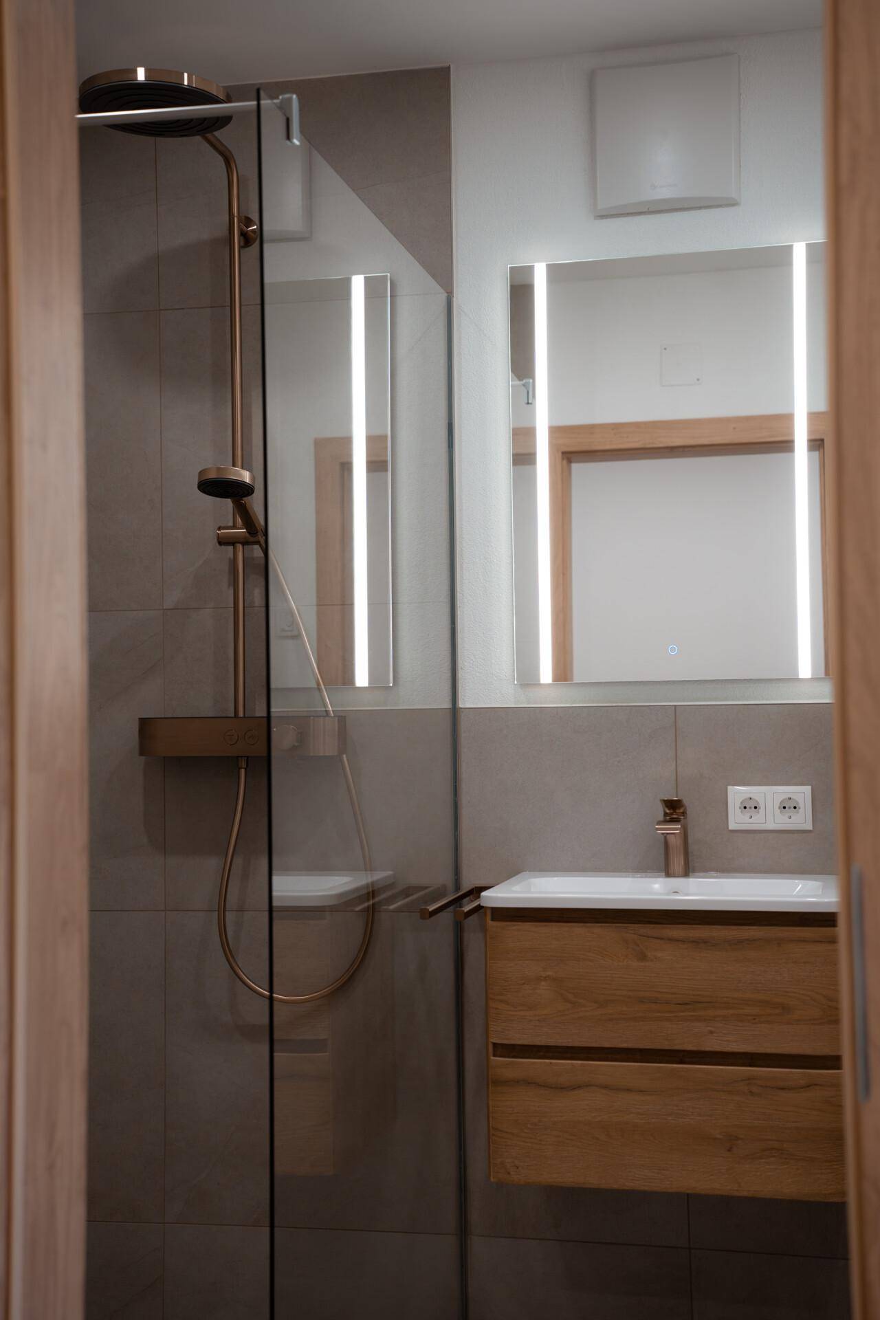 Modernes Badezimmer mit begehbarer Dusche, Einzelwaschbecken und beleuchtetem Spiegel.