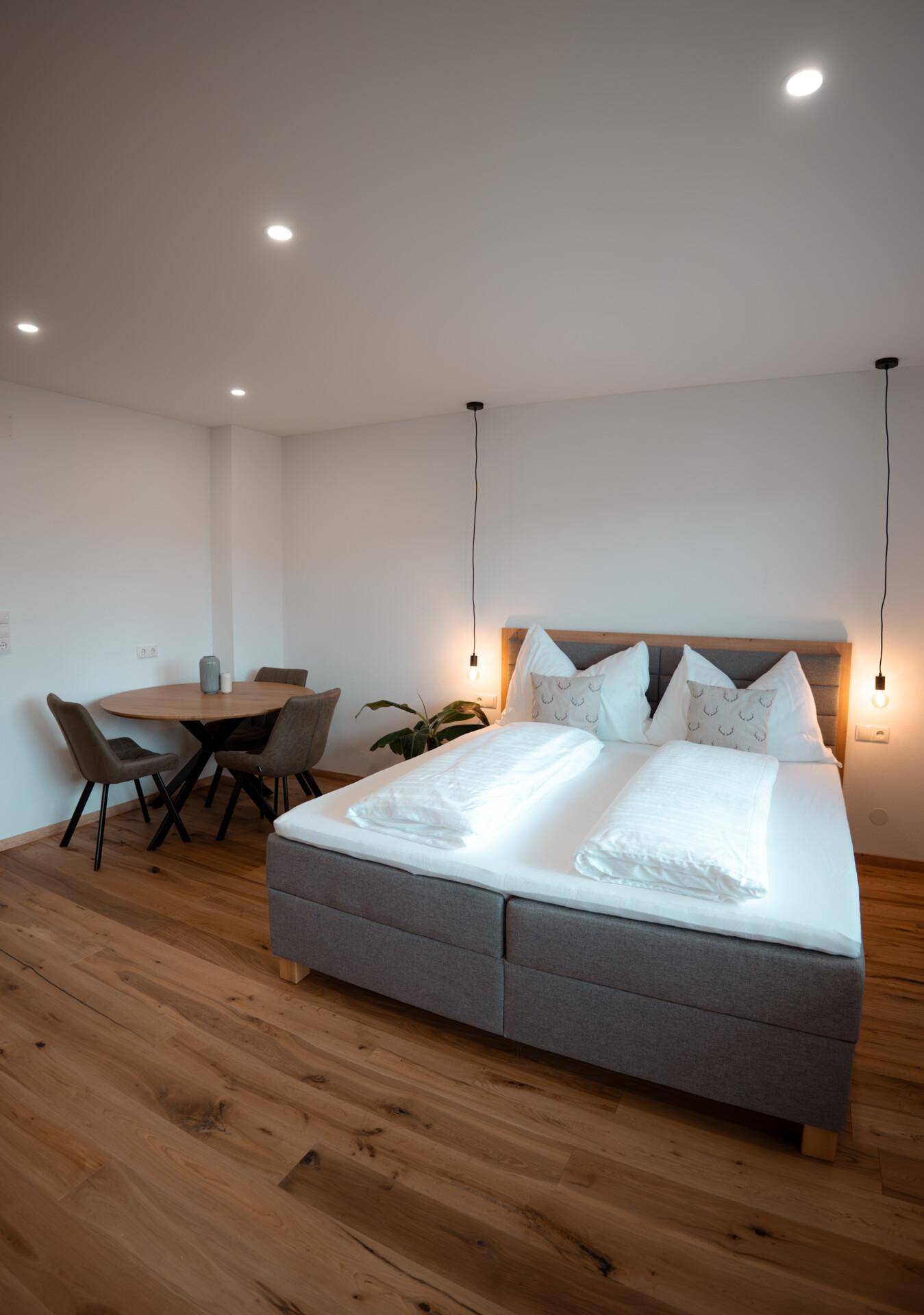 Helles Schlafzimmer mit Doppelbett, Holzboden und einem kleinen Esstisch.