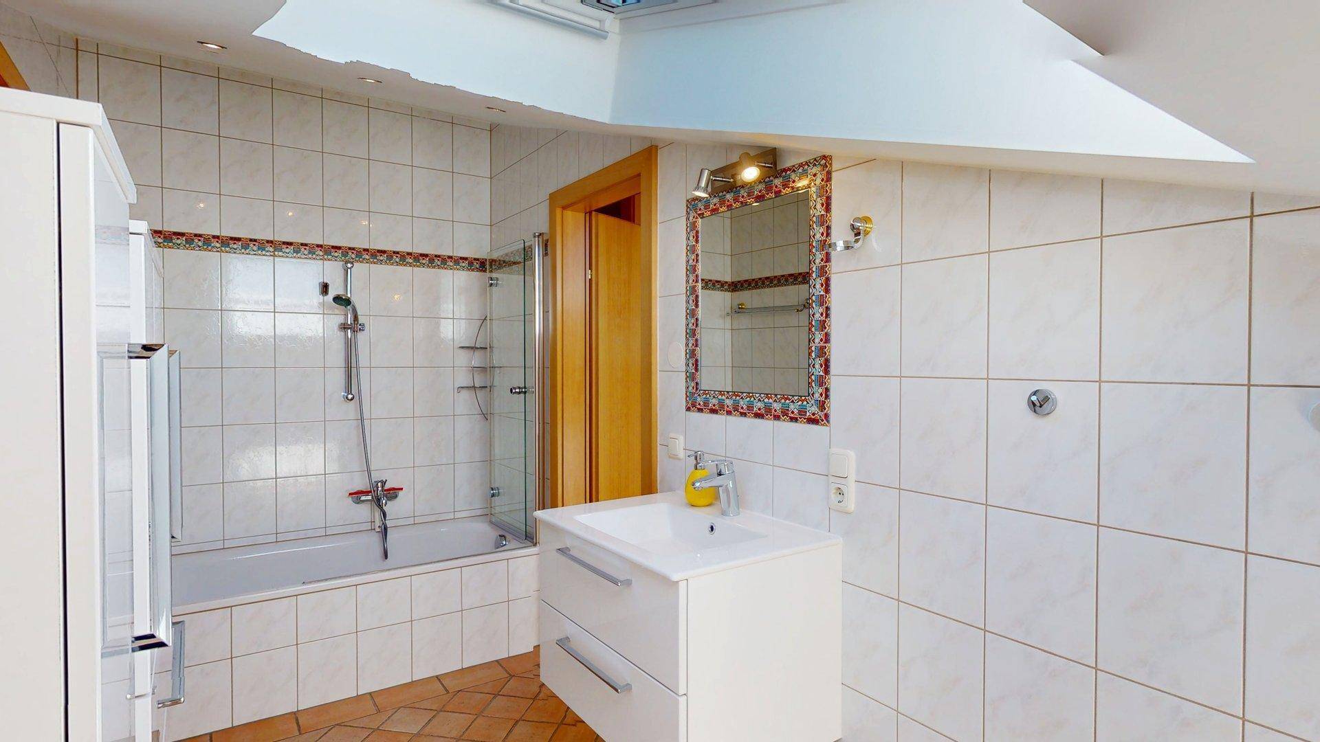 Helles Badezimmer mit Badewanne, Dusche, Waschbecken und Fliesenboden im Dachgeschoss.