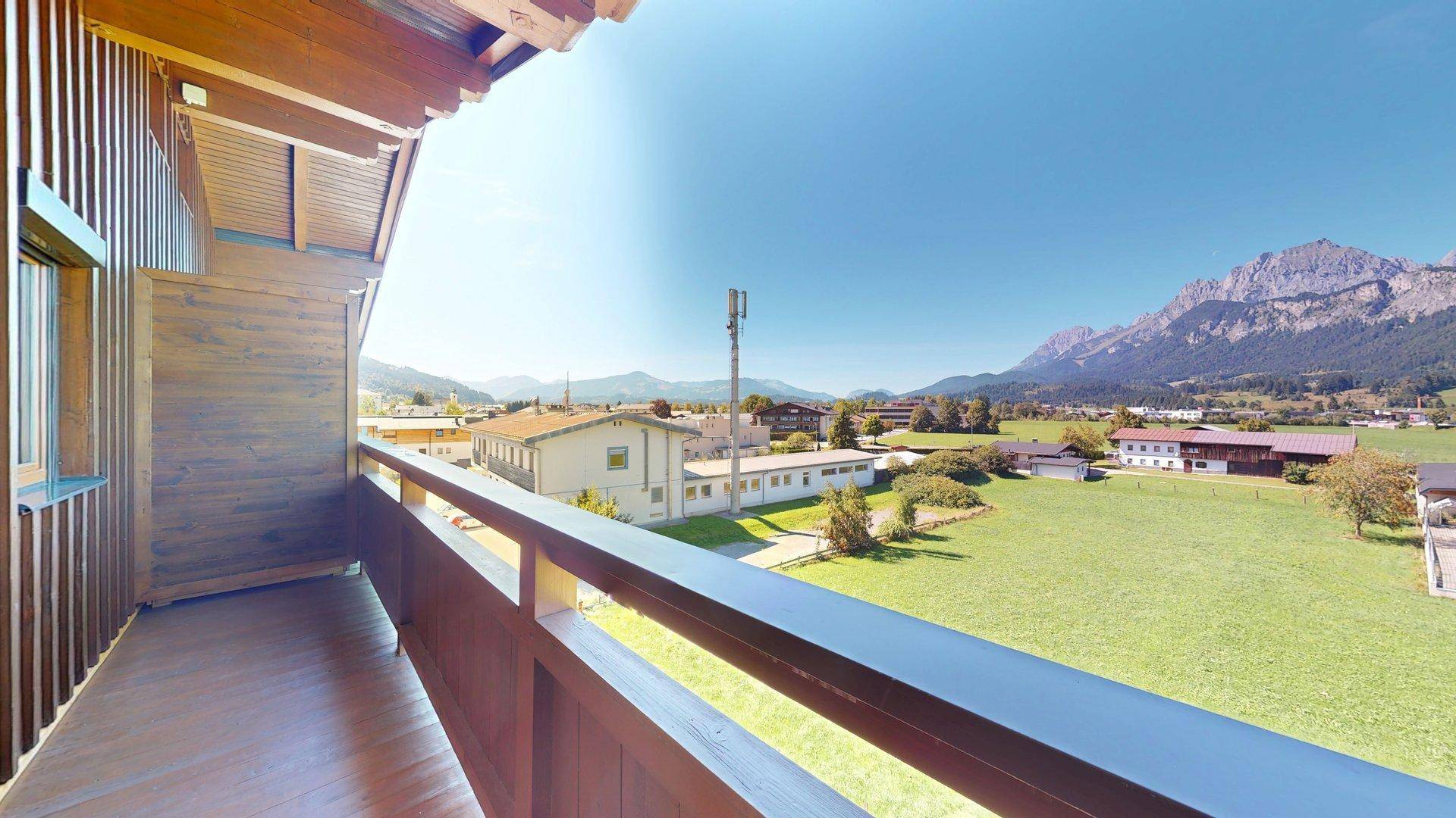 Geräumiger Holzbalkon mit weitem Blick über grüne Felder und die umliegende Berglandschaft.