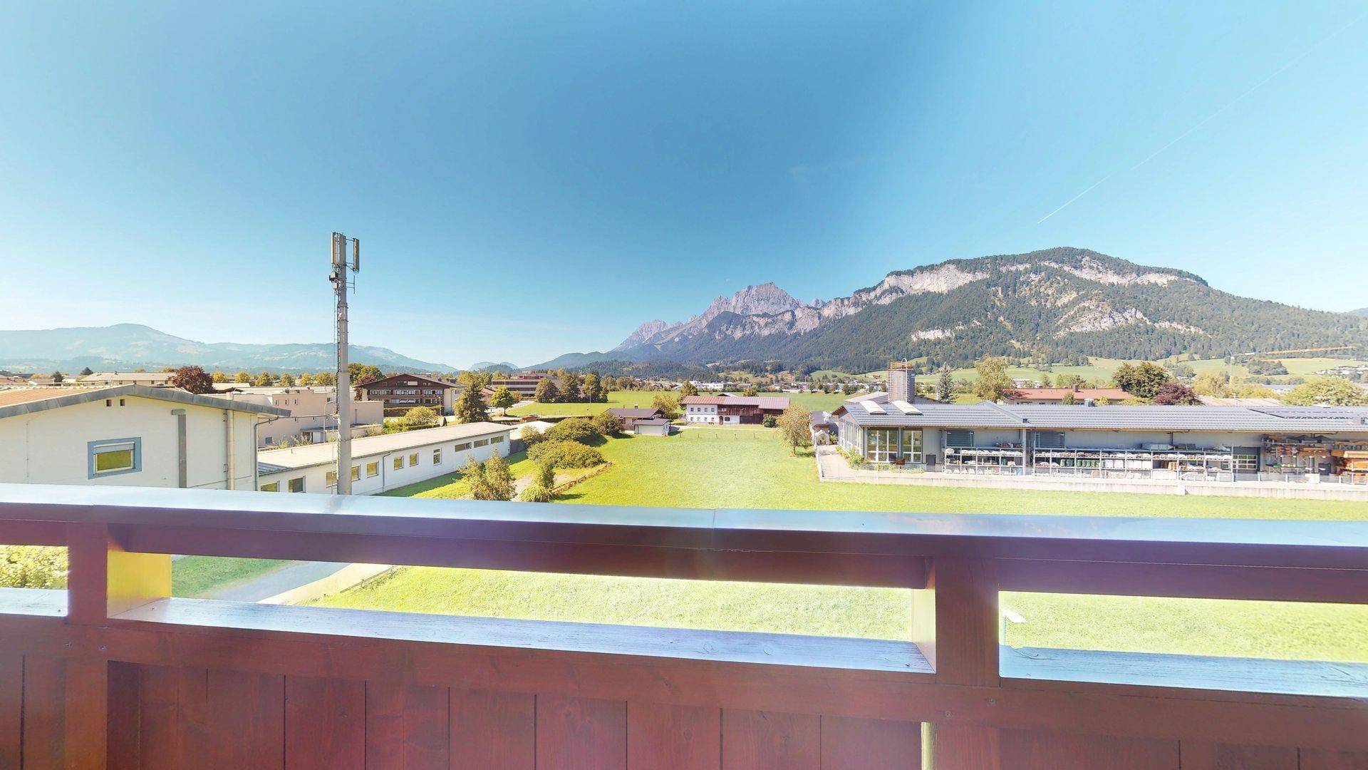 Weitläufiger Ausblick vom Balkon über grüne Wiesen und die beeindruckende Bergkulisse.