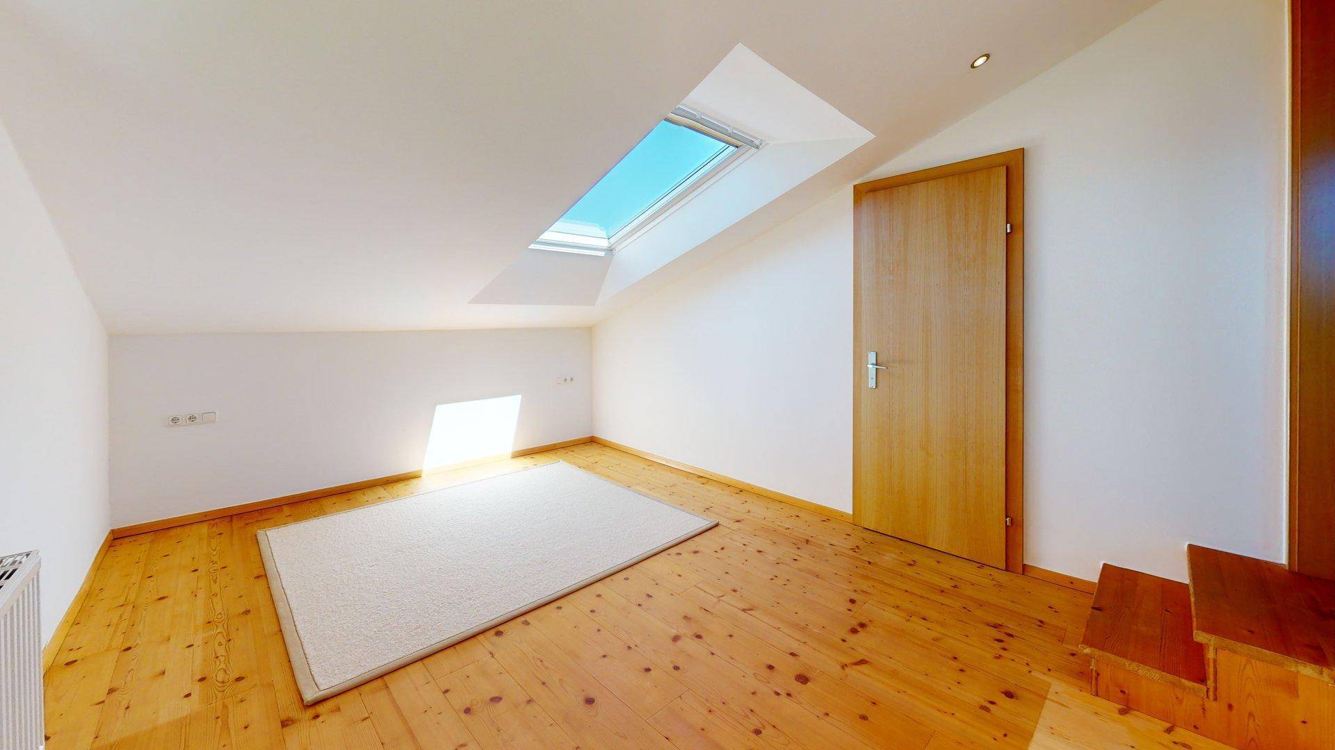 Geräumiges Dachzimmer mit Holzboden, viel Tageslicht durch das Dachfenster und schräger Decke.