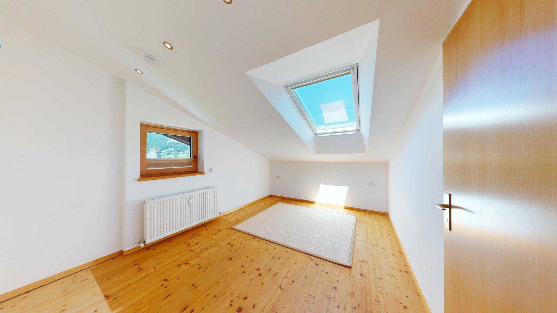 Helles Zimmer im Dachgeschoss mit Holzboden, Dachfenster und schräger Decke.