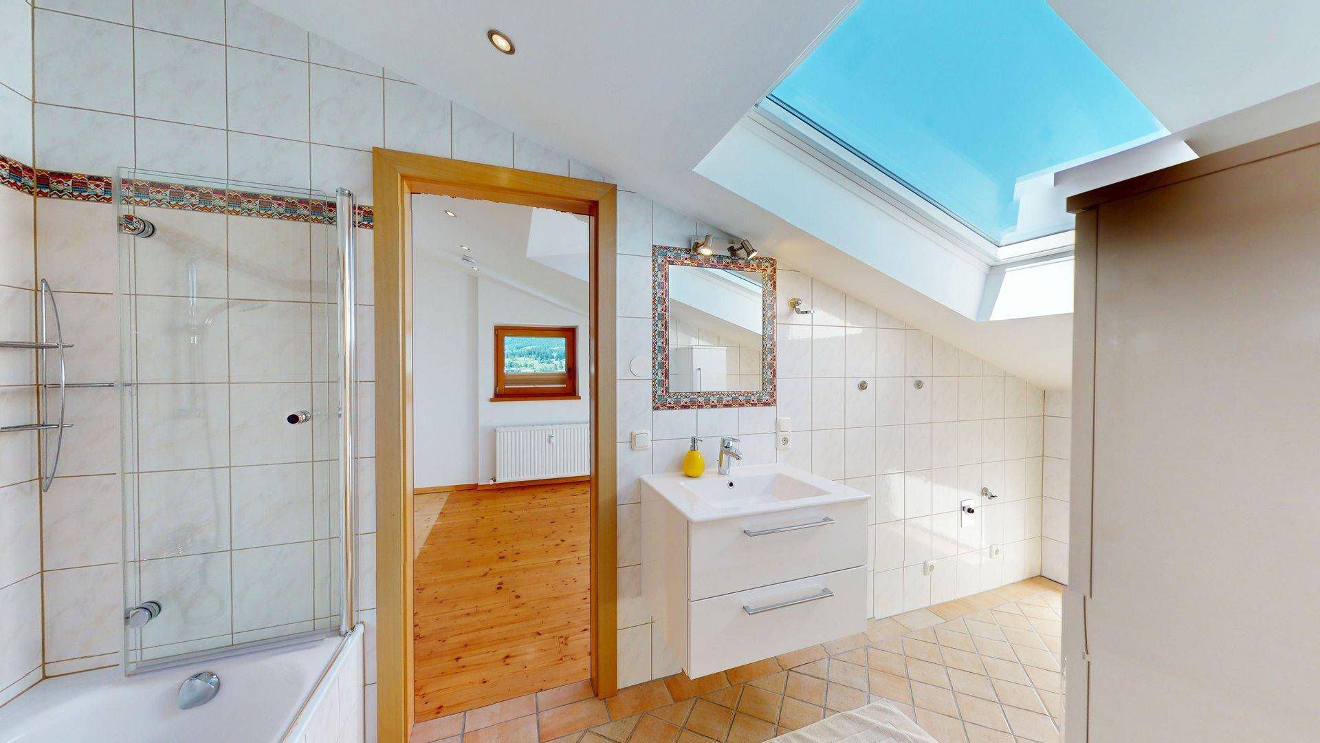 Badezimmer im Dachgeschoss mit Dusche, Waschbecken, Dachfenster und schrägen Wänden.