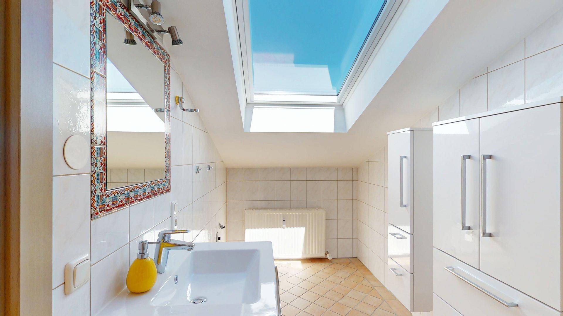 Modernes Badezimmer im Dachgeschoss mit Waschbecken, Spiegelschrank und großem Dachfenster.