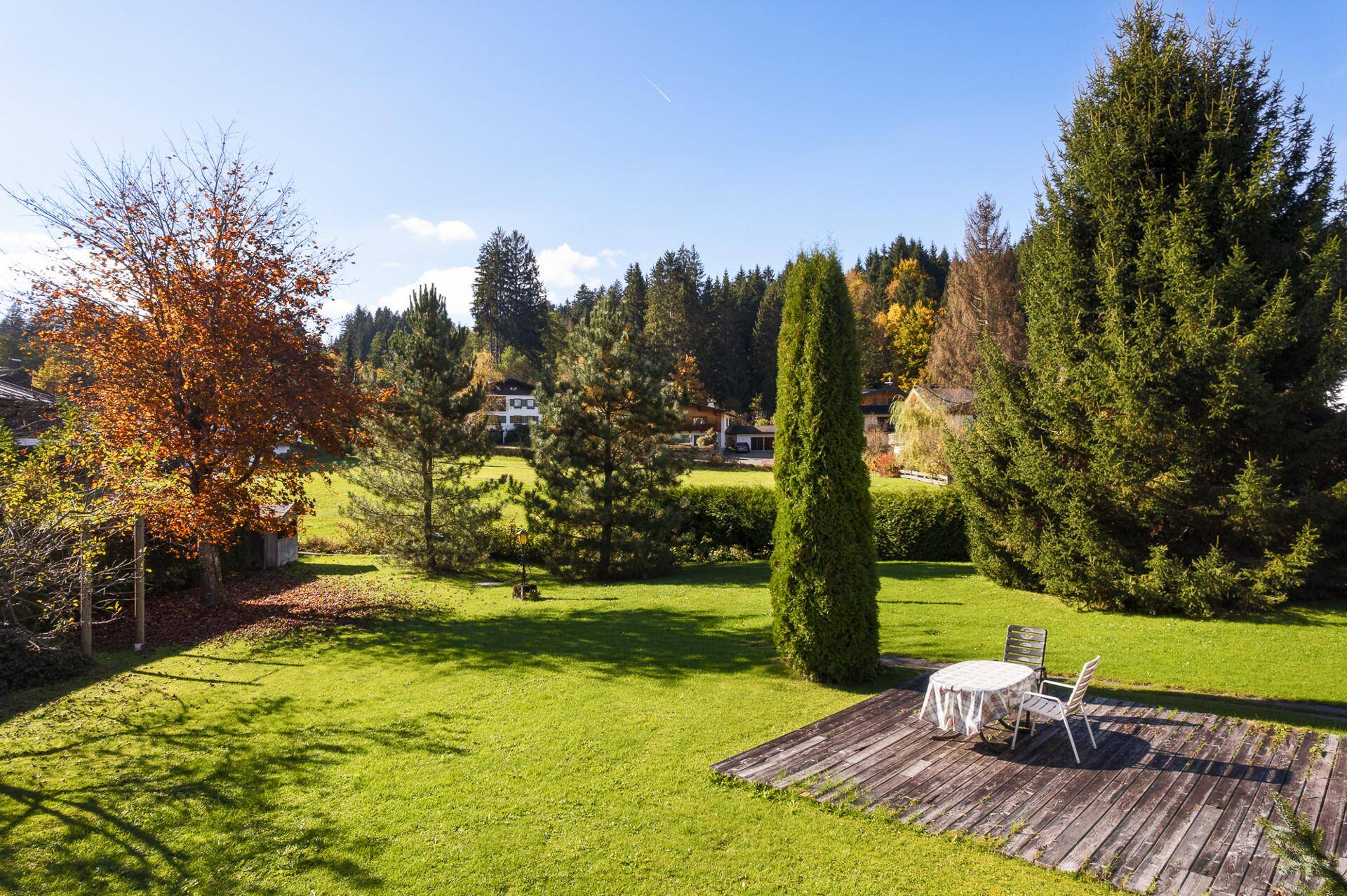 Weitläufiger grüner Garten mit einer Holzterrasse und einem kleinen Tisch mit Stühlen für entspannte Stunden.