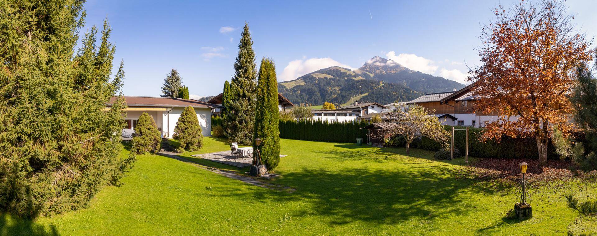 Panoramablick auf den weitläufigen Garten mit Rasen, hohen Bäumen und beeindruckendem Bergpanorama im Hintergrund.