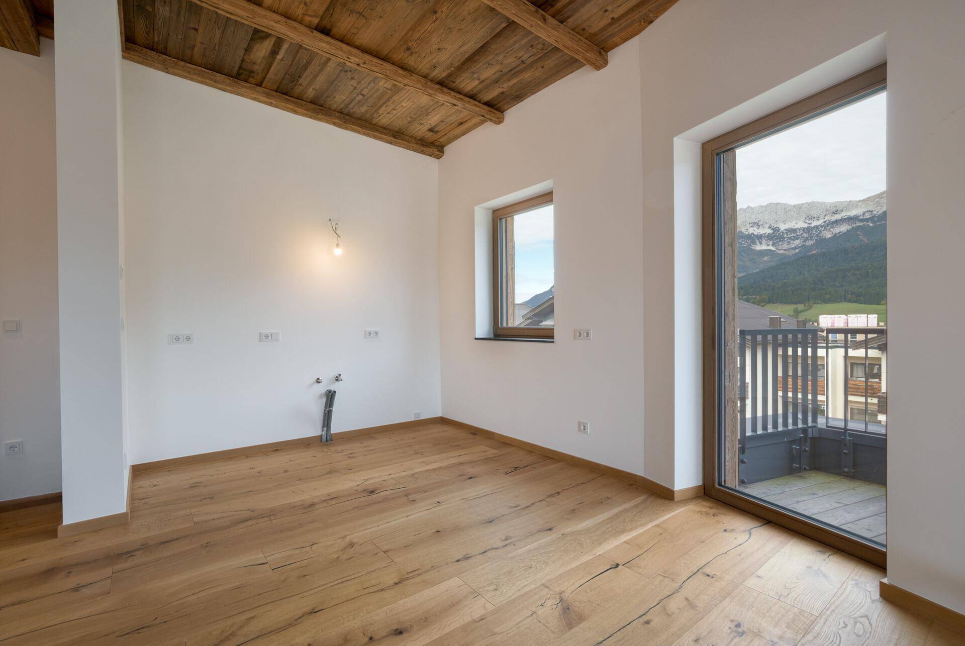 Leerer Raum mit Holzboden, Holzbalkendecke und Zugang zu einem Balkon mit Bergblick.